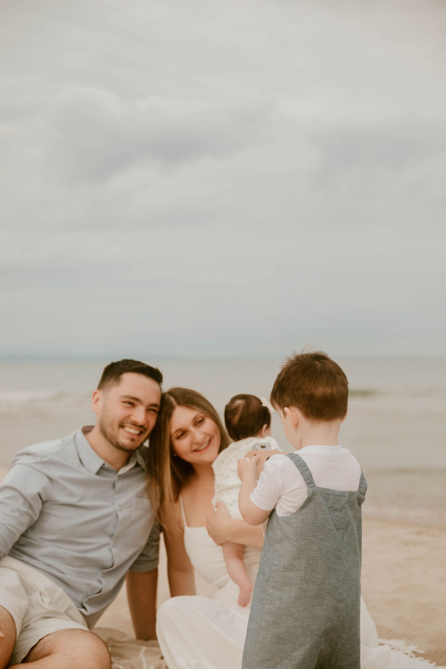 Family sitting together on sandy beach under cloudy sky.