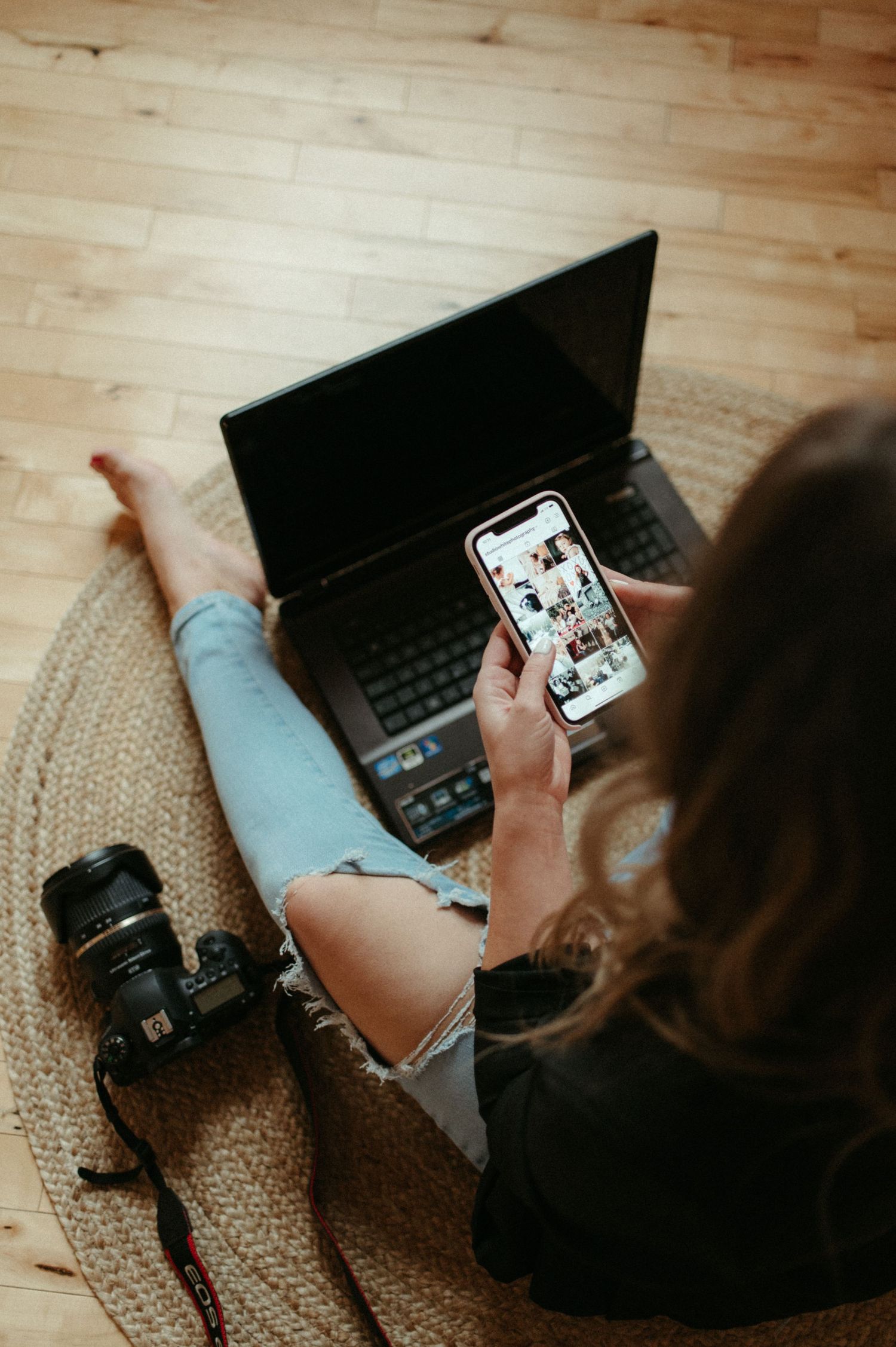 Person browsing social media on phone while sitting with laptop on woven rug.