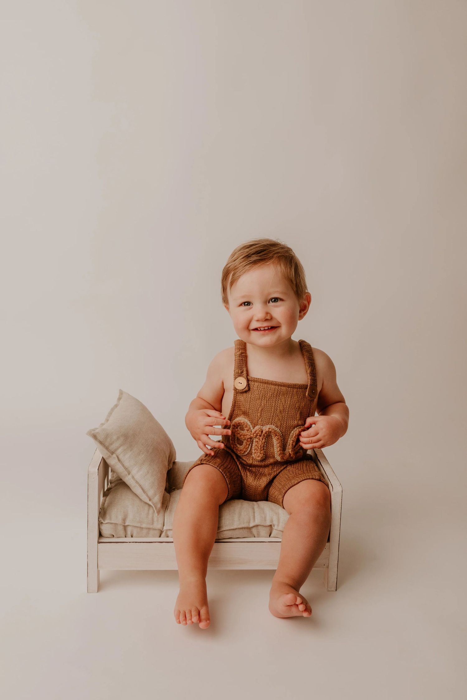 A series of minimalist baby photos showing a small child sitting on a light colored bench in brown clothing.