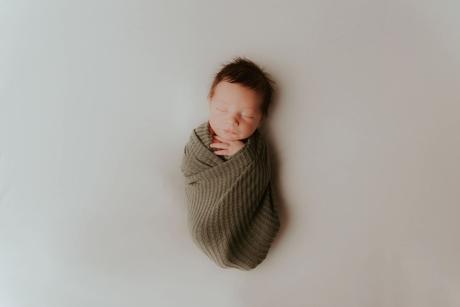 Overhead view of someone in a knit sweater lying on white bedding.