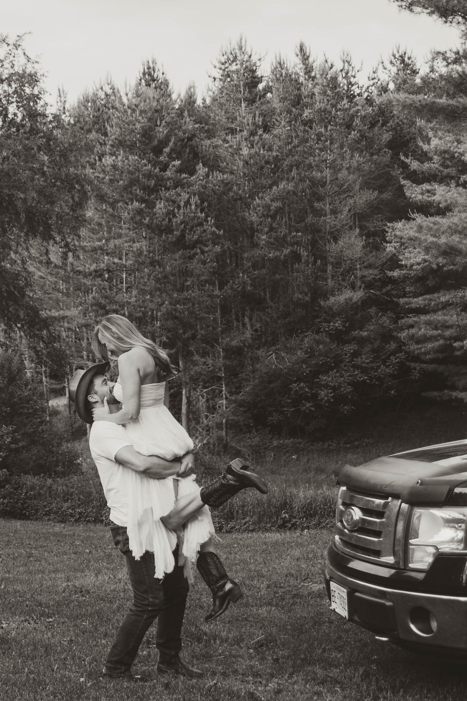Black and white photos of a romantic moment by a parked car in a field.