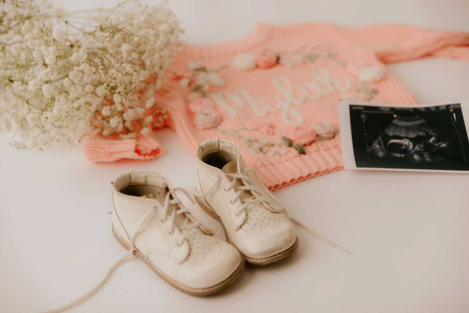 A vintage-style photo collage shows white baby shoes and polaroid photos arranged on a light textured background.