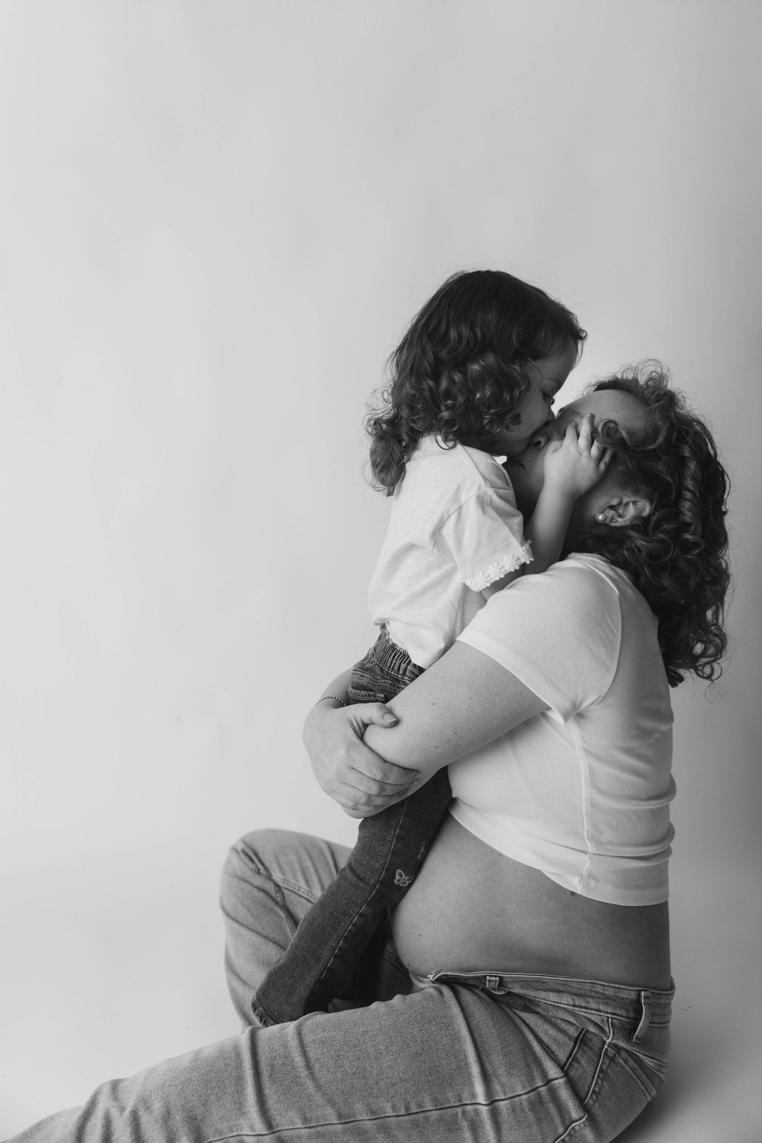 Black and white photo of a pregnant woman sitting and embracing her young child in a tender maternity portrait.