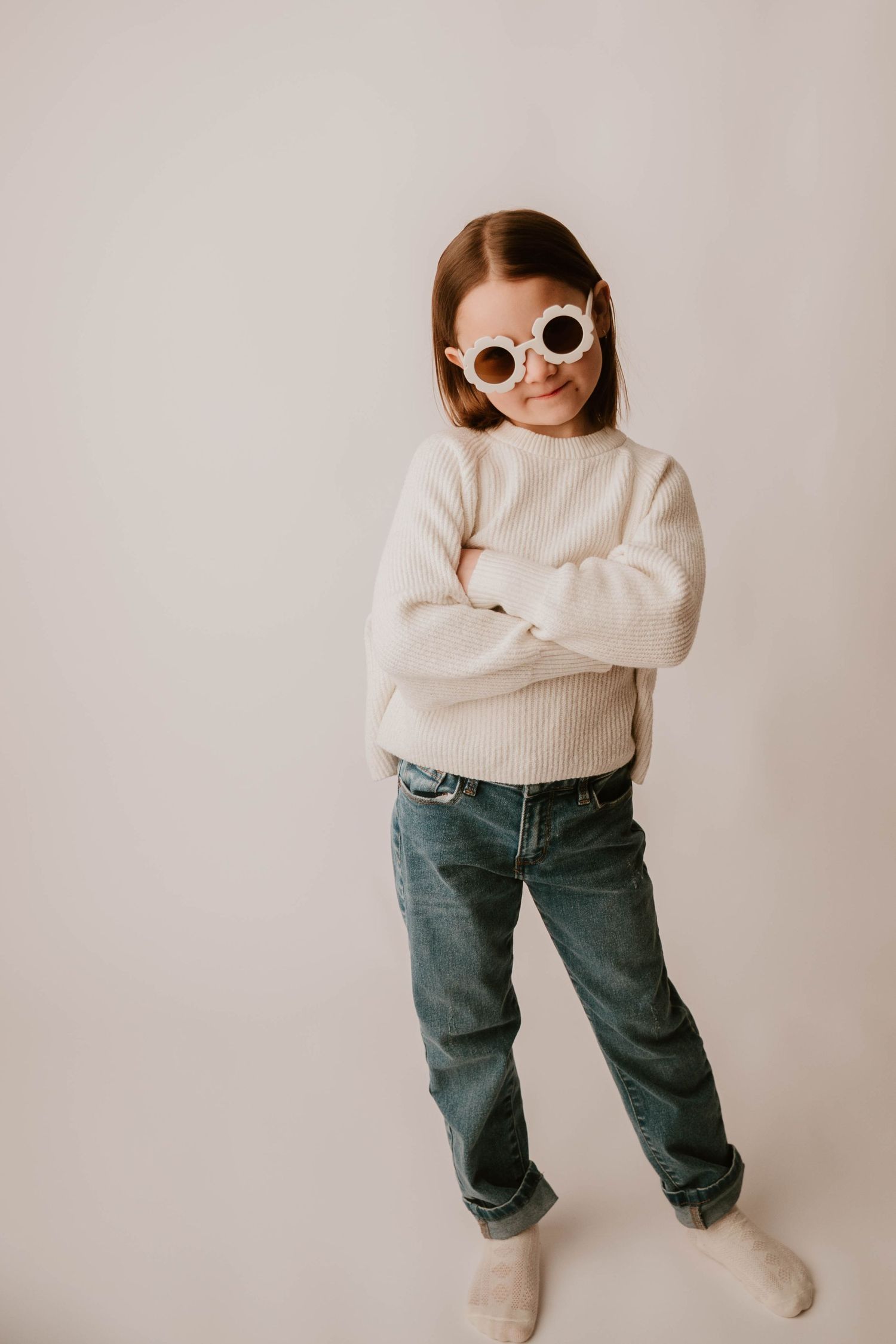 A series of minimalist fashion photos showing white sweater, blue jeans and sunglasses against neutral backdrop.