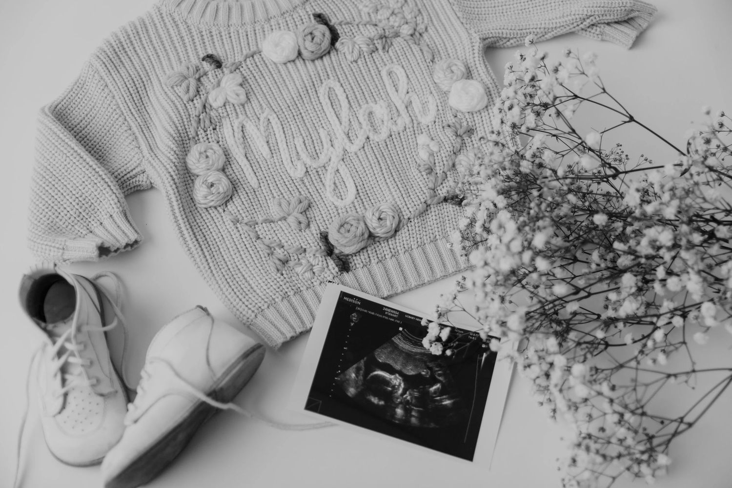Flatlay of knitted sweater with delicate flowers and accessories in monochrome.