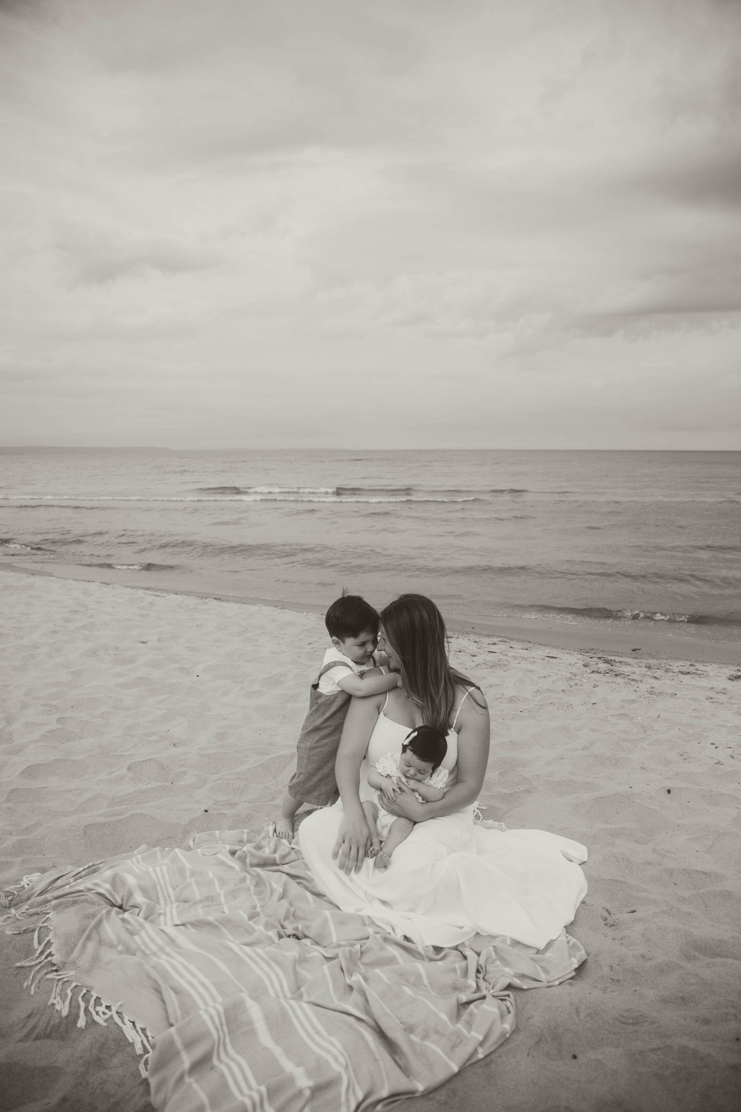 A white dress flows in the breeze as figures embrace on a cloudy beach.