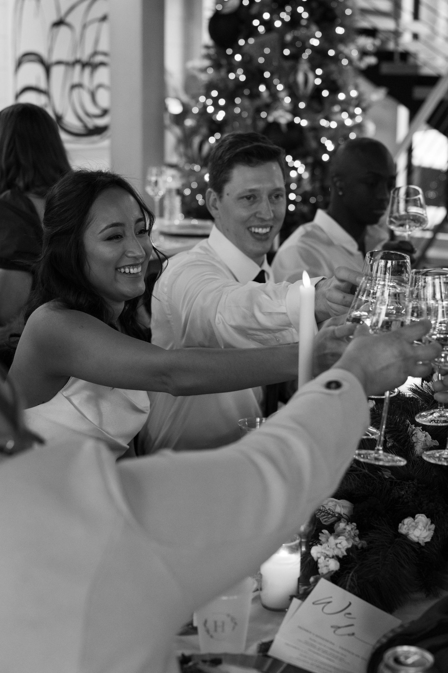 Black and white photo of smiling guests toasting with wine glasses at an elegant Christmas dinner party.