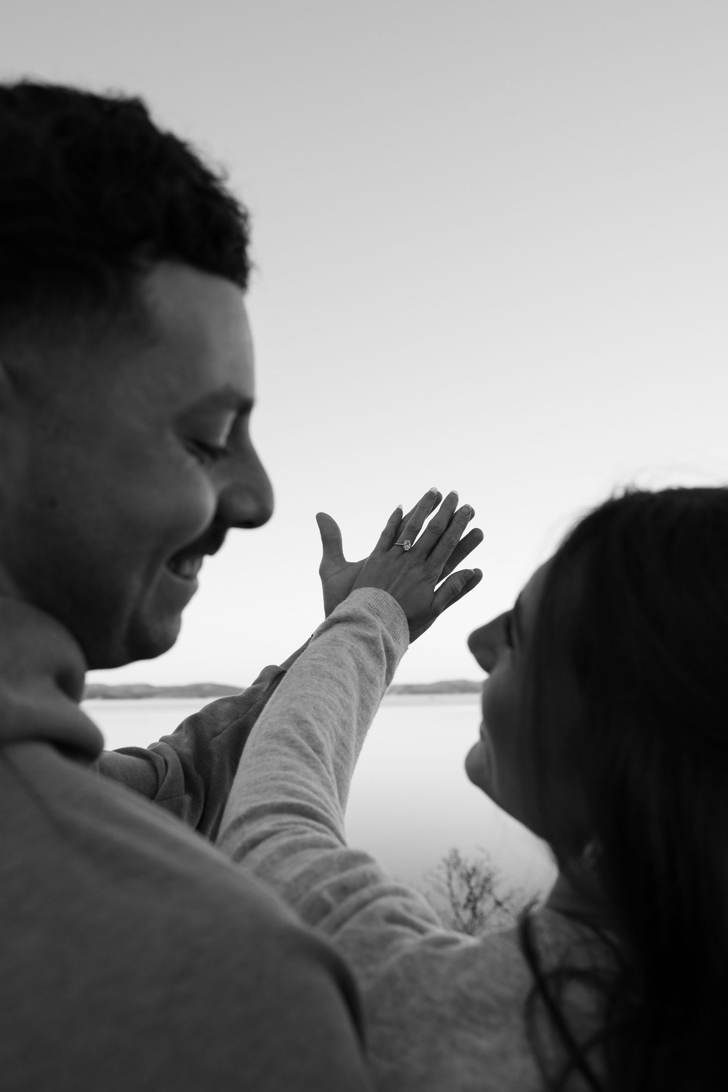 Black and white photo of a smiling couple near a lake, woman touching man's face tenderly.