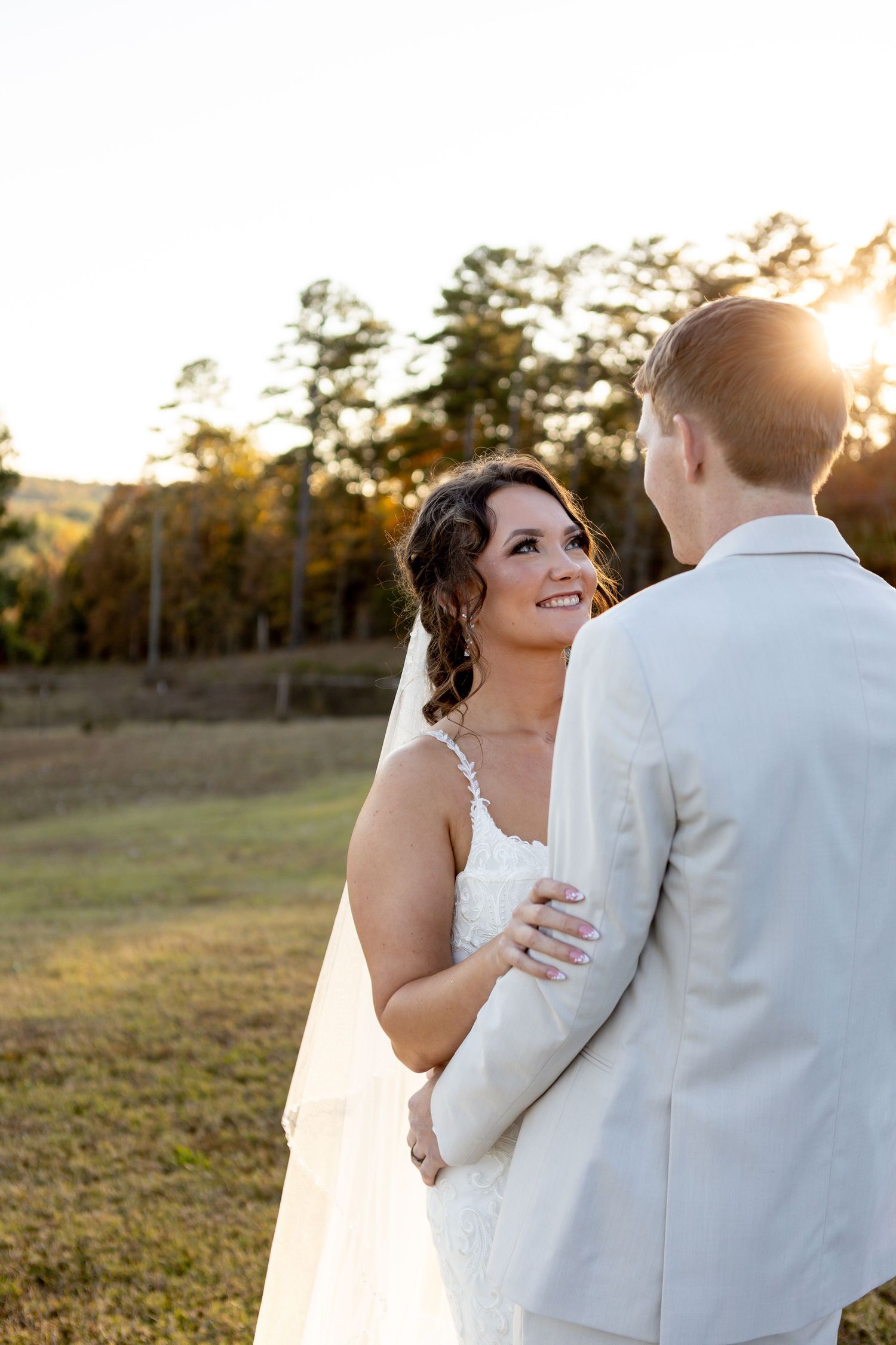 A romantic wedding couple shares an intimate moment at sunset in a grassy field.