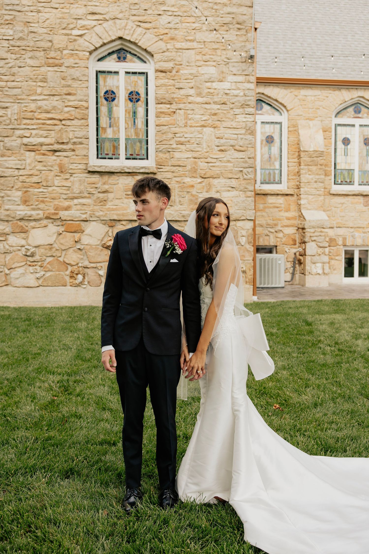 Bride and groom holding hands outside stone church with stained glass windows.