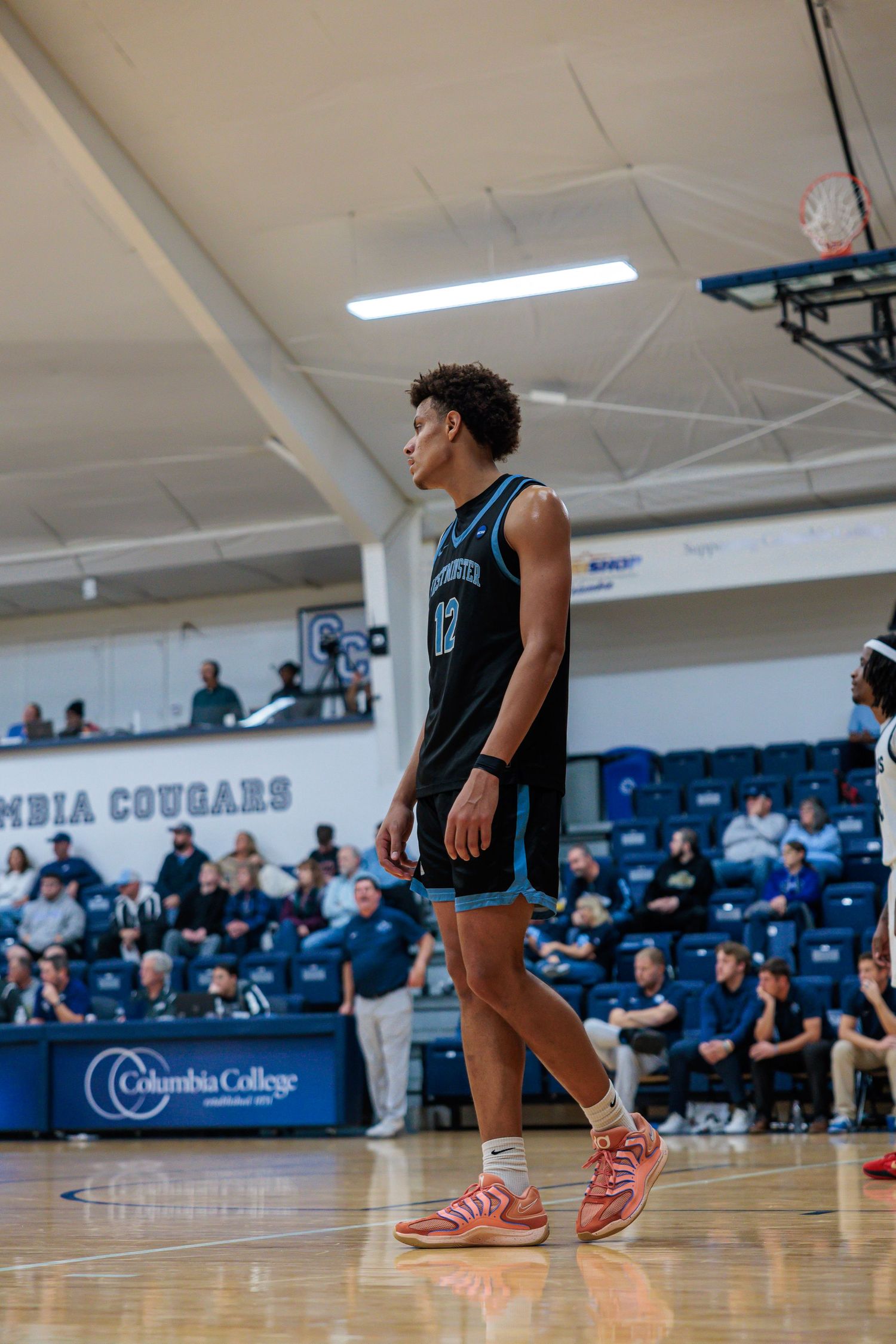 Basketball player in dark uniform standing on the court at Columbia College Cougars arena during a game.
