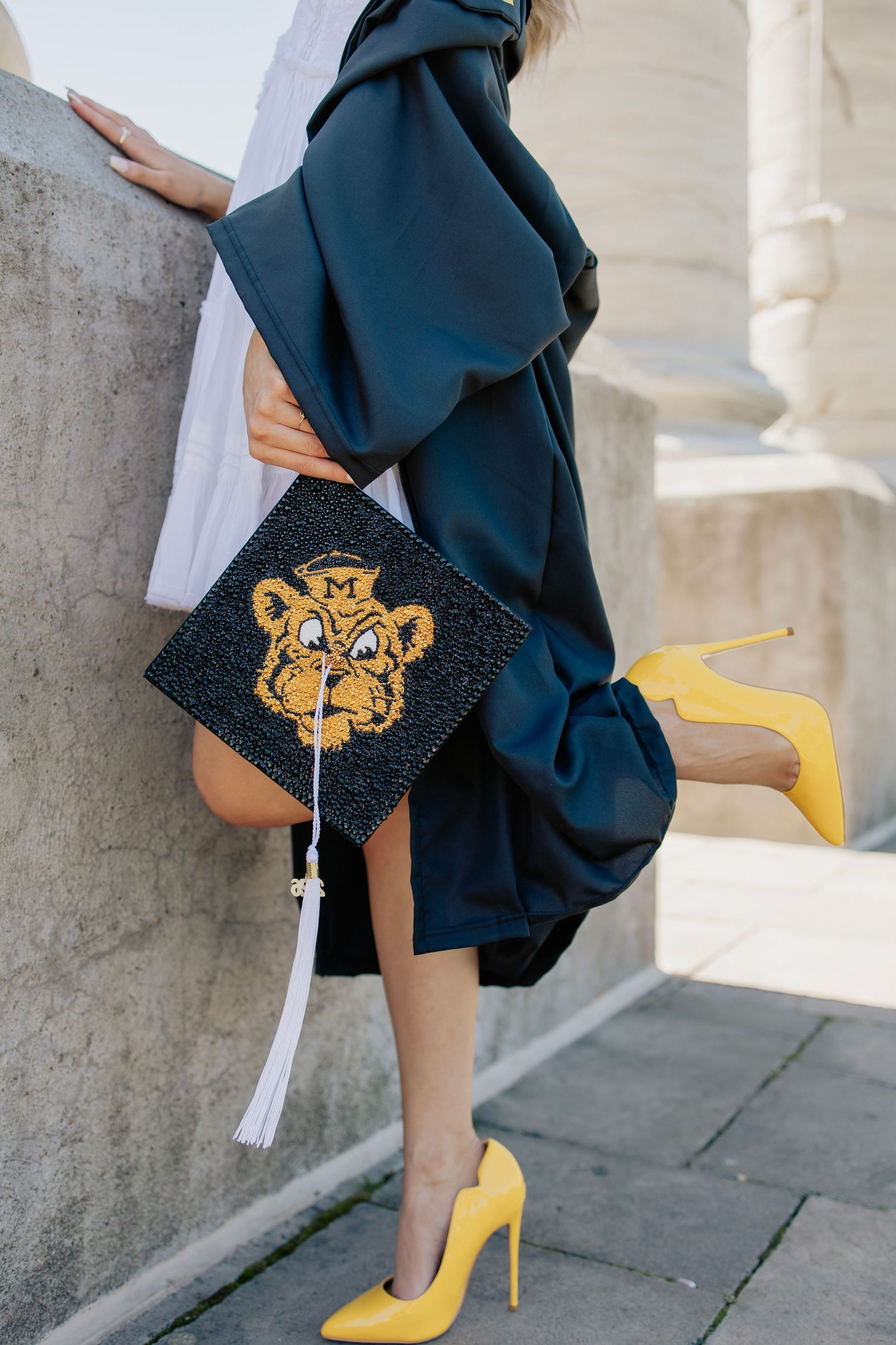 Close-up of decorated tiger graduation cap and yellow heels against navy graduation gown.