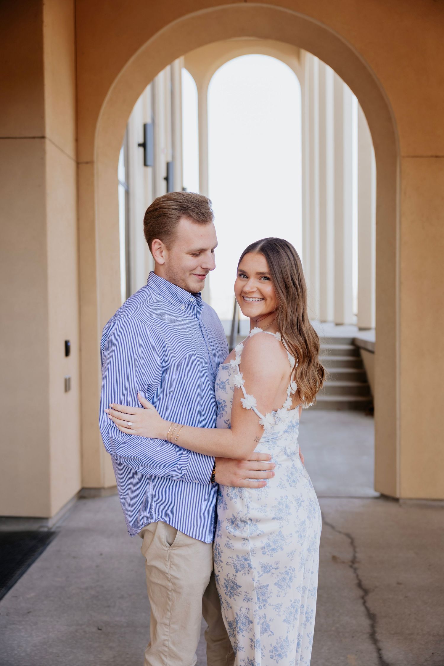 Couple embracing under an arched walkway with columns during a warm golden hour engagement session.