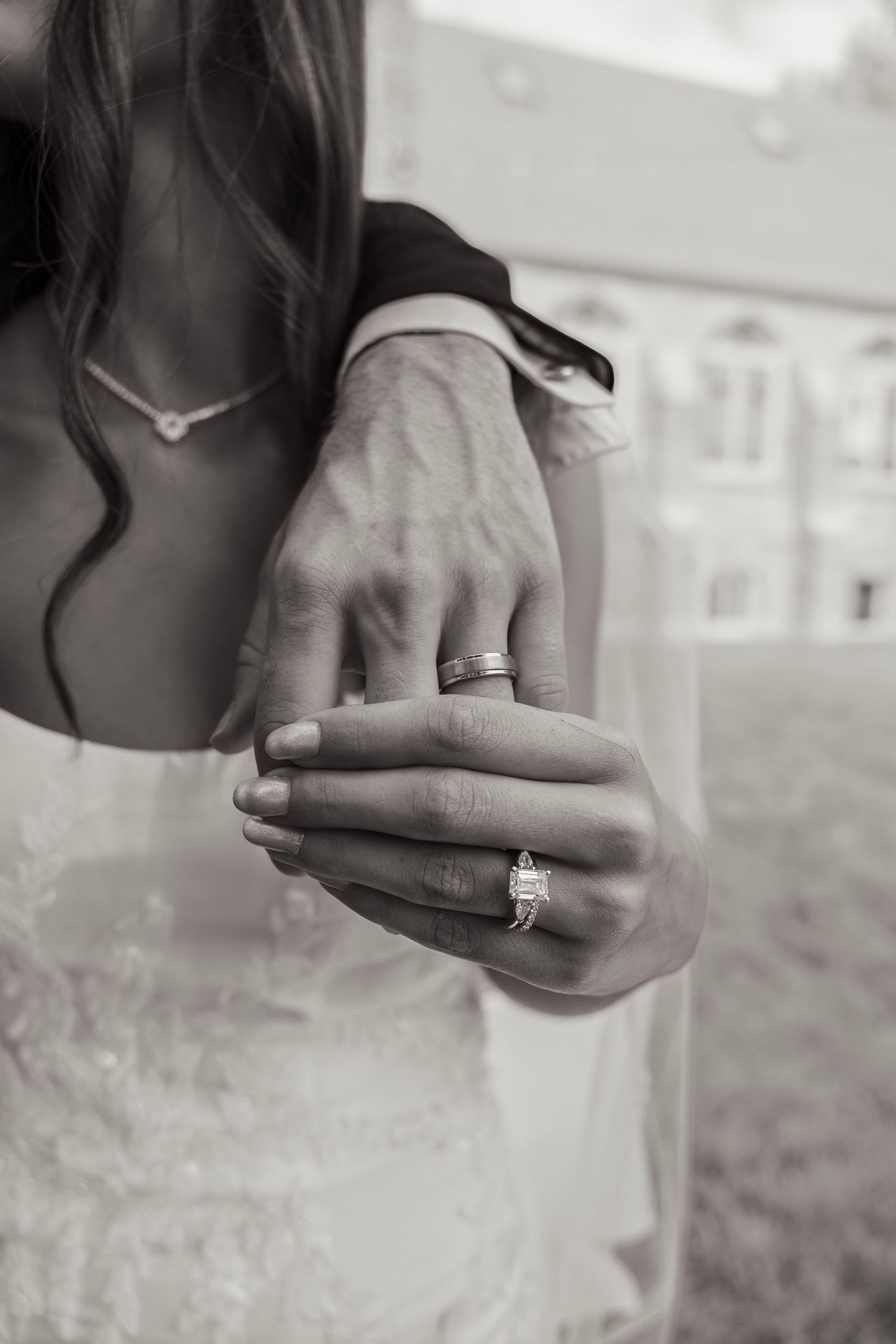 Black and white close-up of bride and grooms hands showing wedding rings and engagement ring.