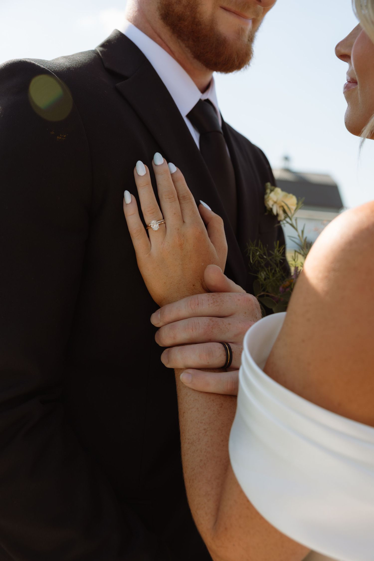 Bride and groom showing wedding rings, woman in white dress resting hand on mans arm in black suit.
