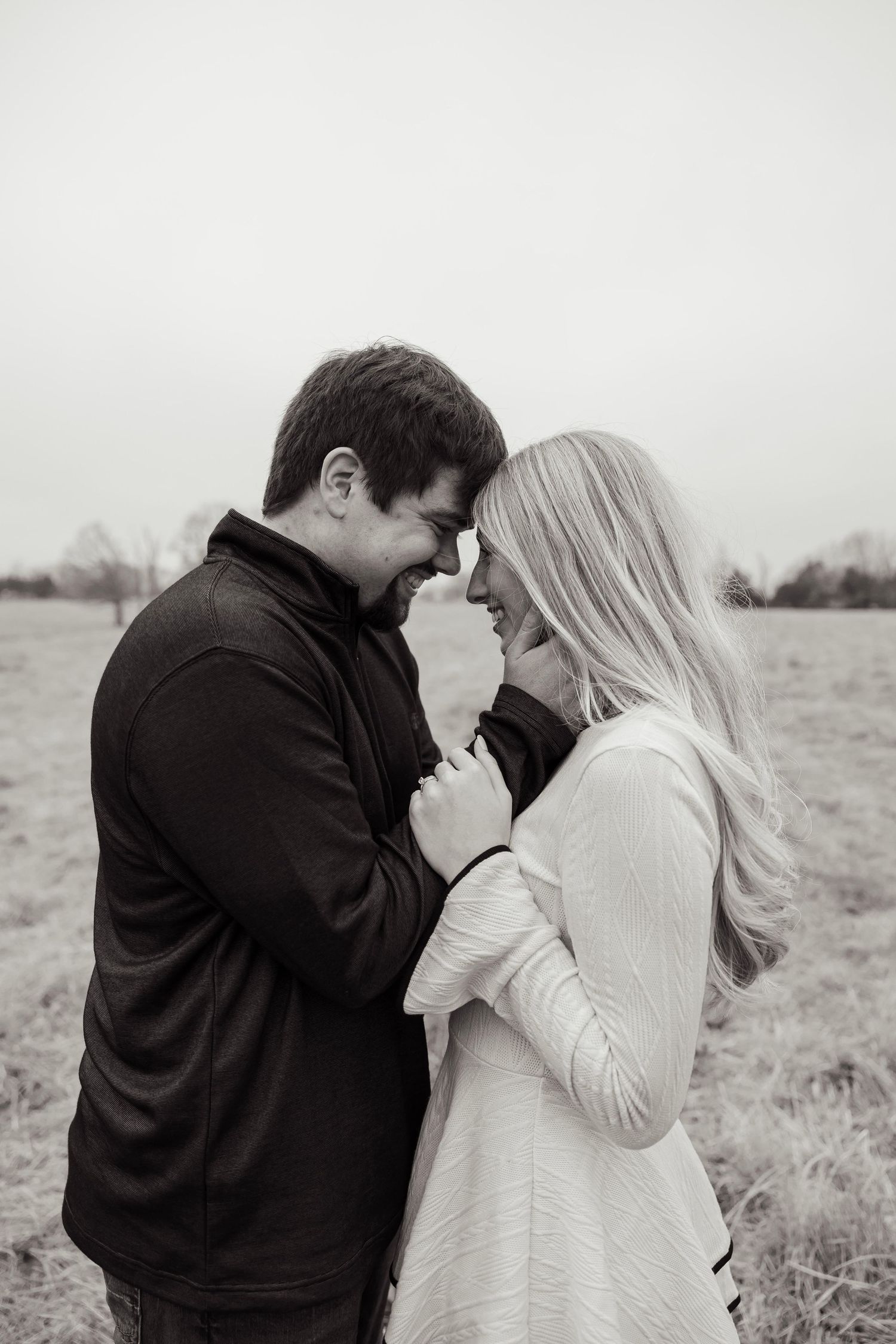Black and white photo of couple smiling and touching foreheads tenderly in an open field.