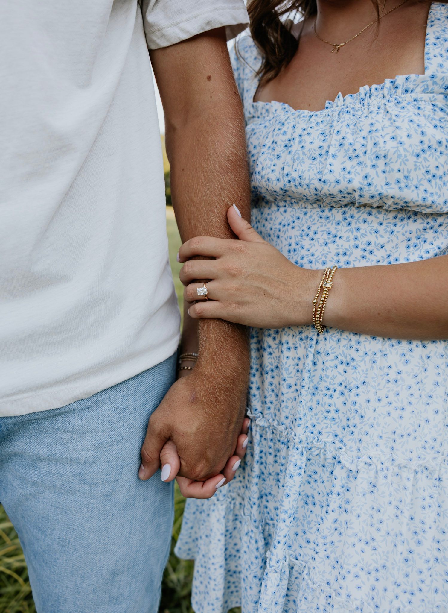 Close-up of a couple holding hands, woman wearing an engagement ring and gold bracelet.