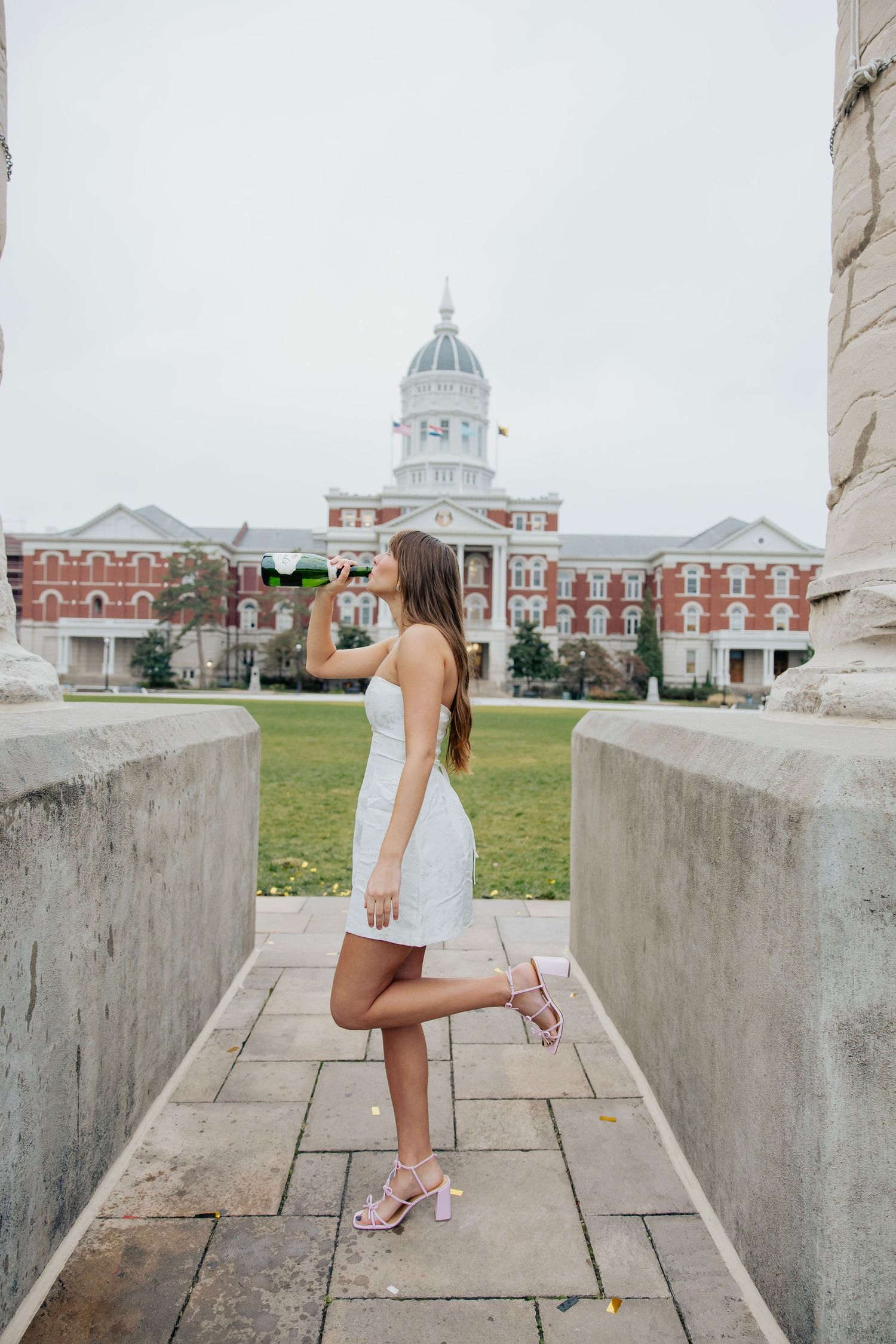 Young woman in white dress holding diploma near university building columns.