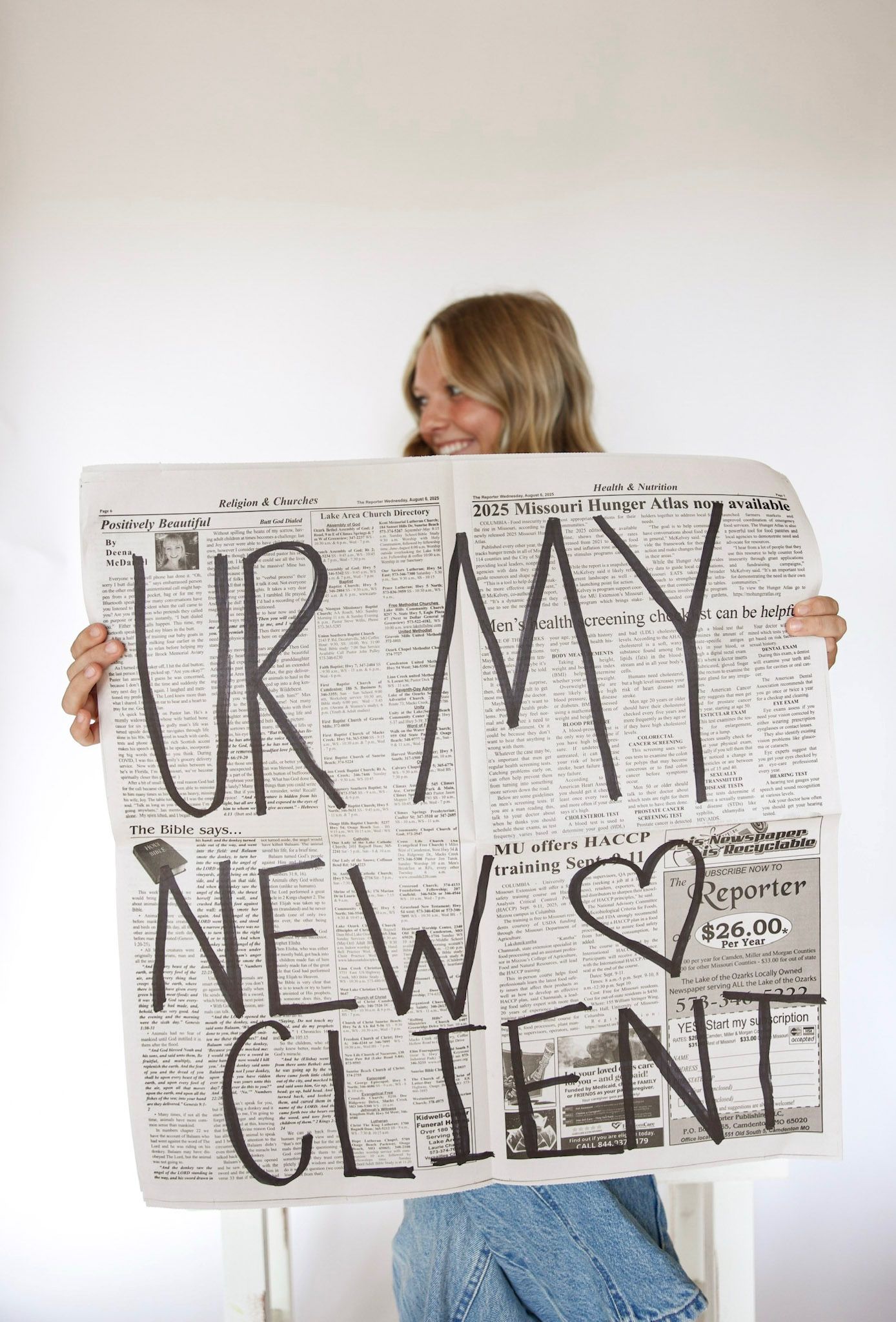 Smiling blonde woman holding newspaper with bold text reading UR MY NEW CLIENT.