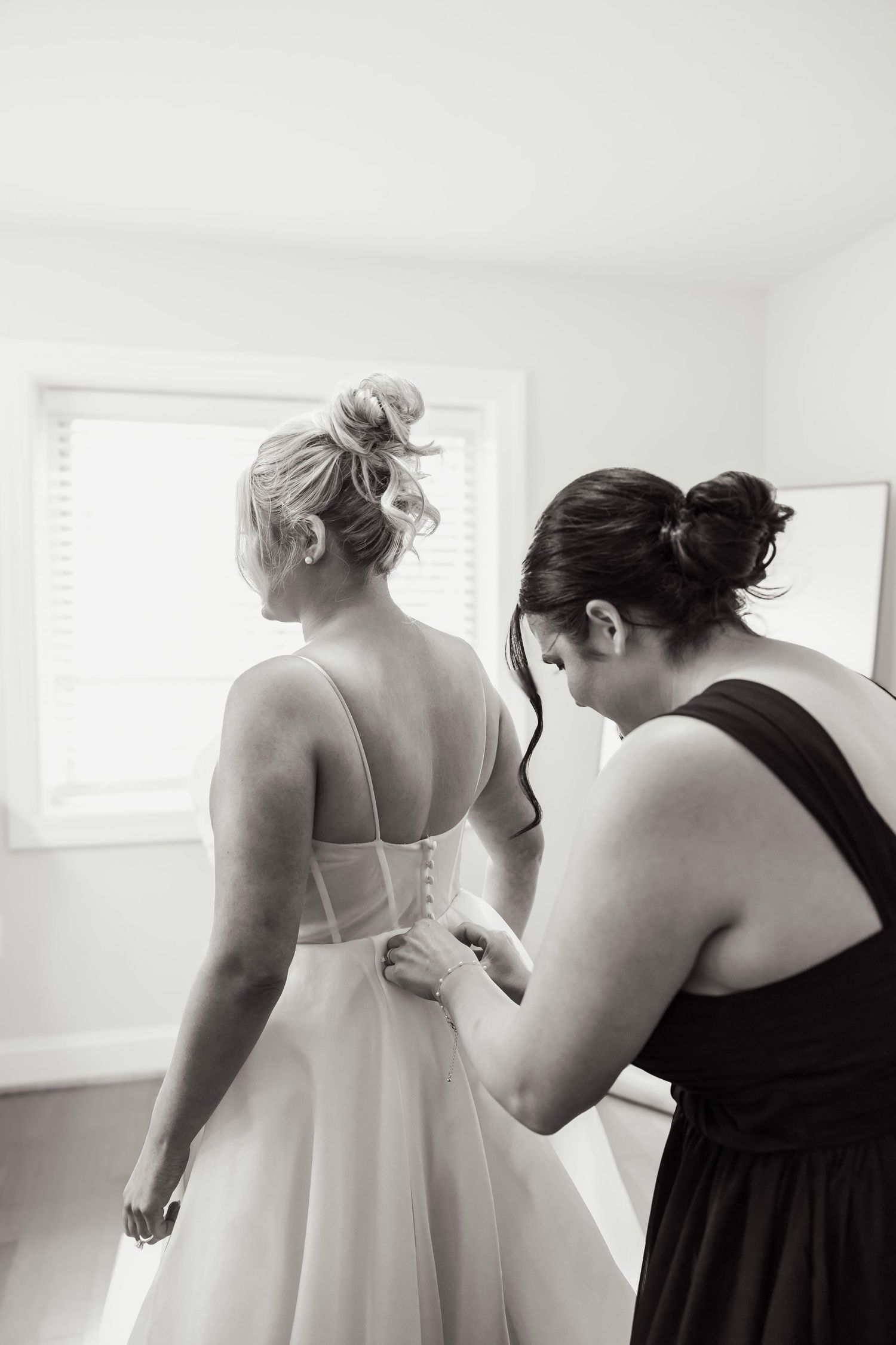 Bridesmaid helping bride button up wedding dress in black and white photo.
