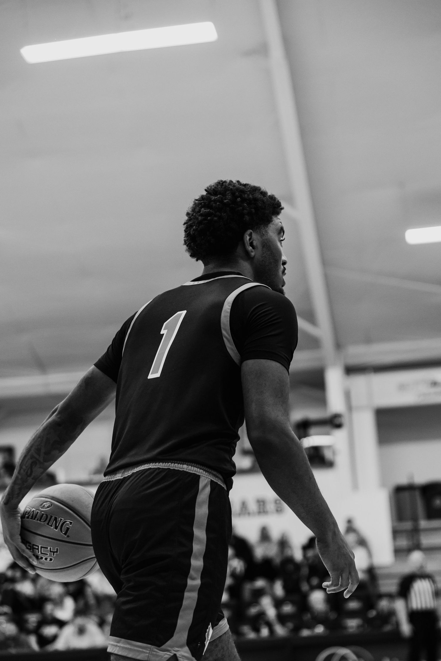 Black and white photo of basketball player number 1 dribbling ball during indoor game.