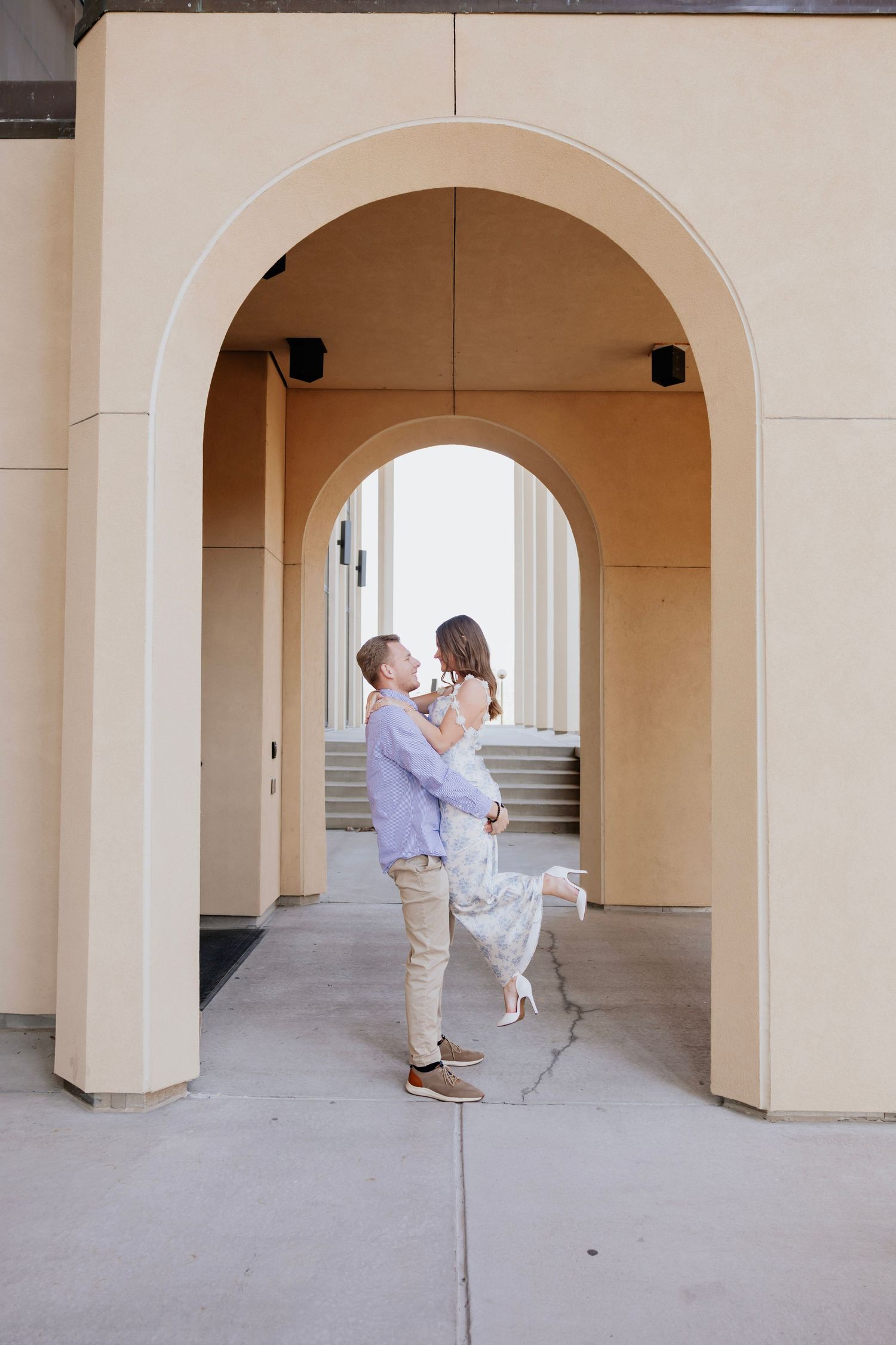 Couple sharing a romantic moment under elegant arched doorway, man lifting woman joyfully.