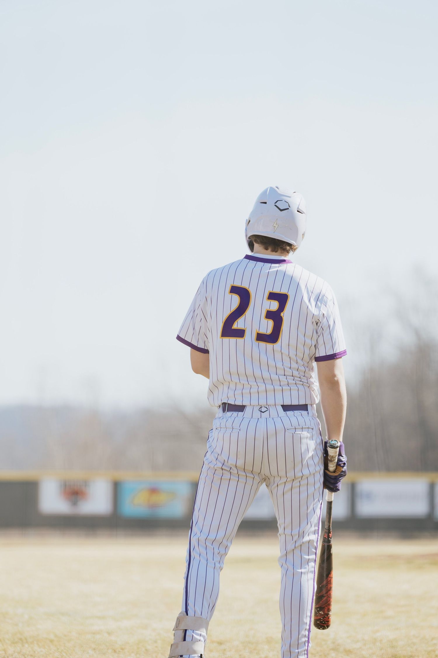 Baseball player wearing number 23 white pinstripe uniform holding a bat viewed from behind on the field.