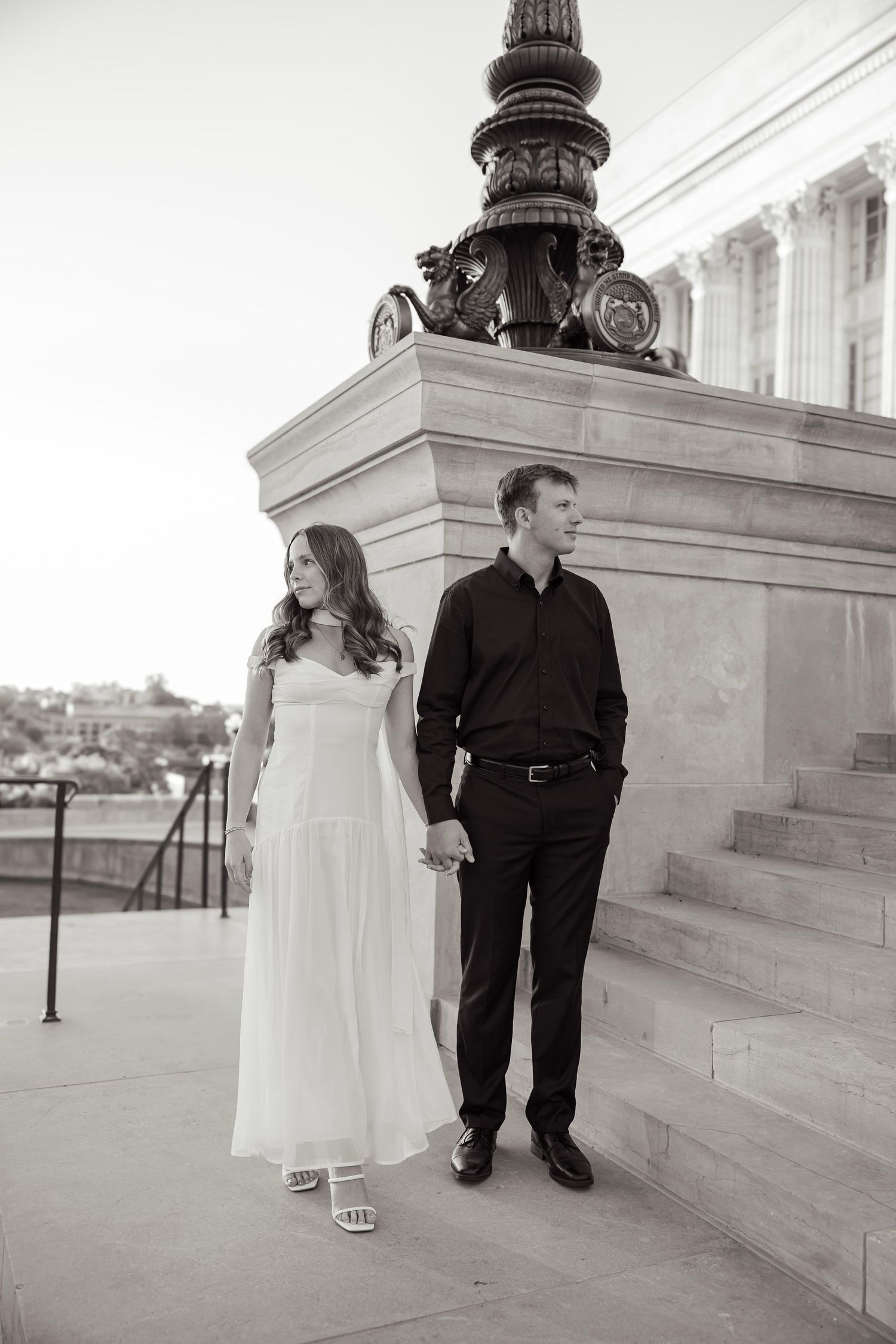 Black and white photo of couple holding hands near an ornate lamp post at a neoclassical building.