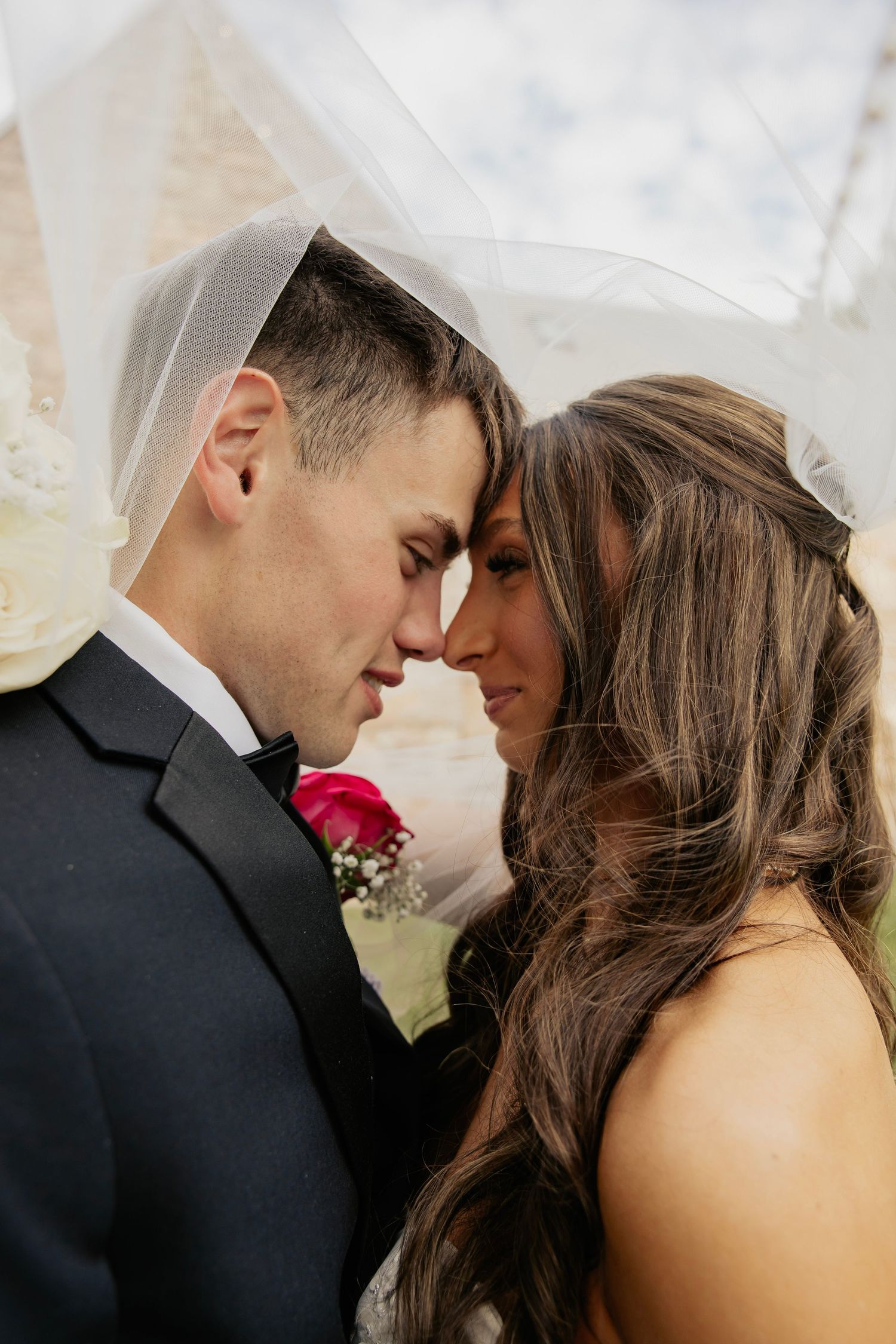 Bride and groom sharing an intimate forehead touch moment under the wedding veil.