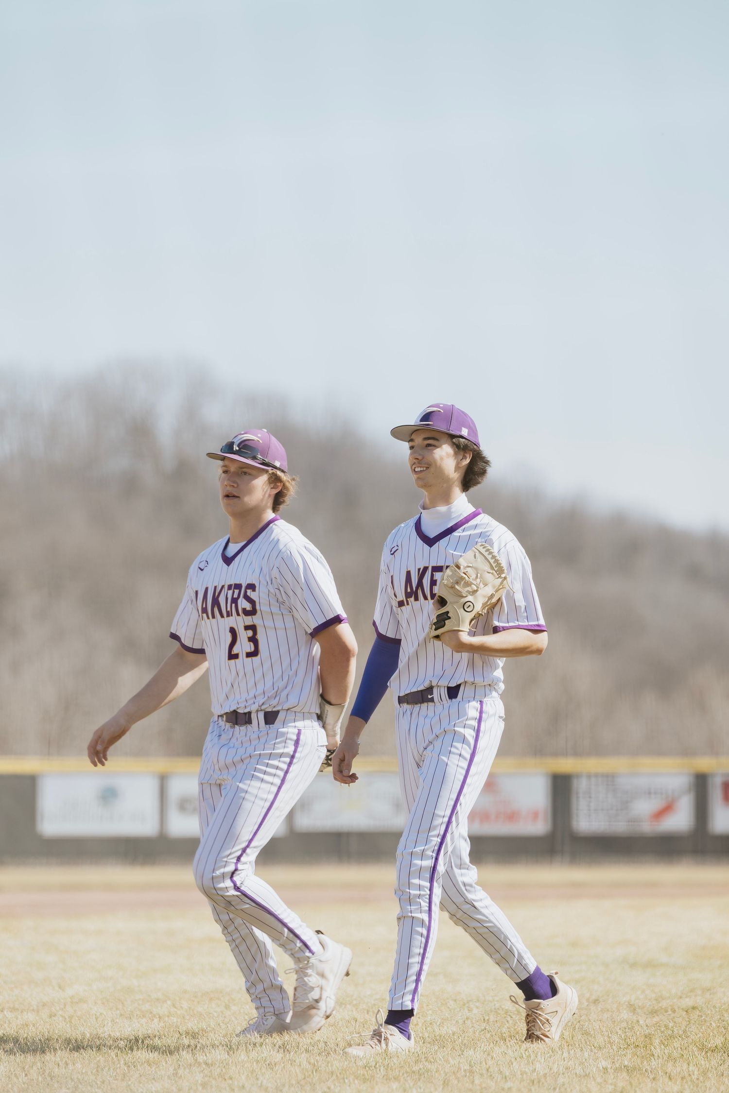 Two Lakers baseball players in white pinstripe uniforms numbered 23 walking together on the outfield grass.