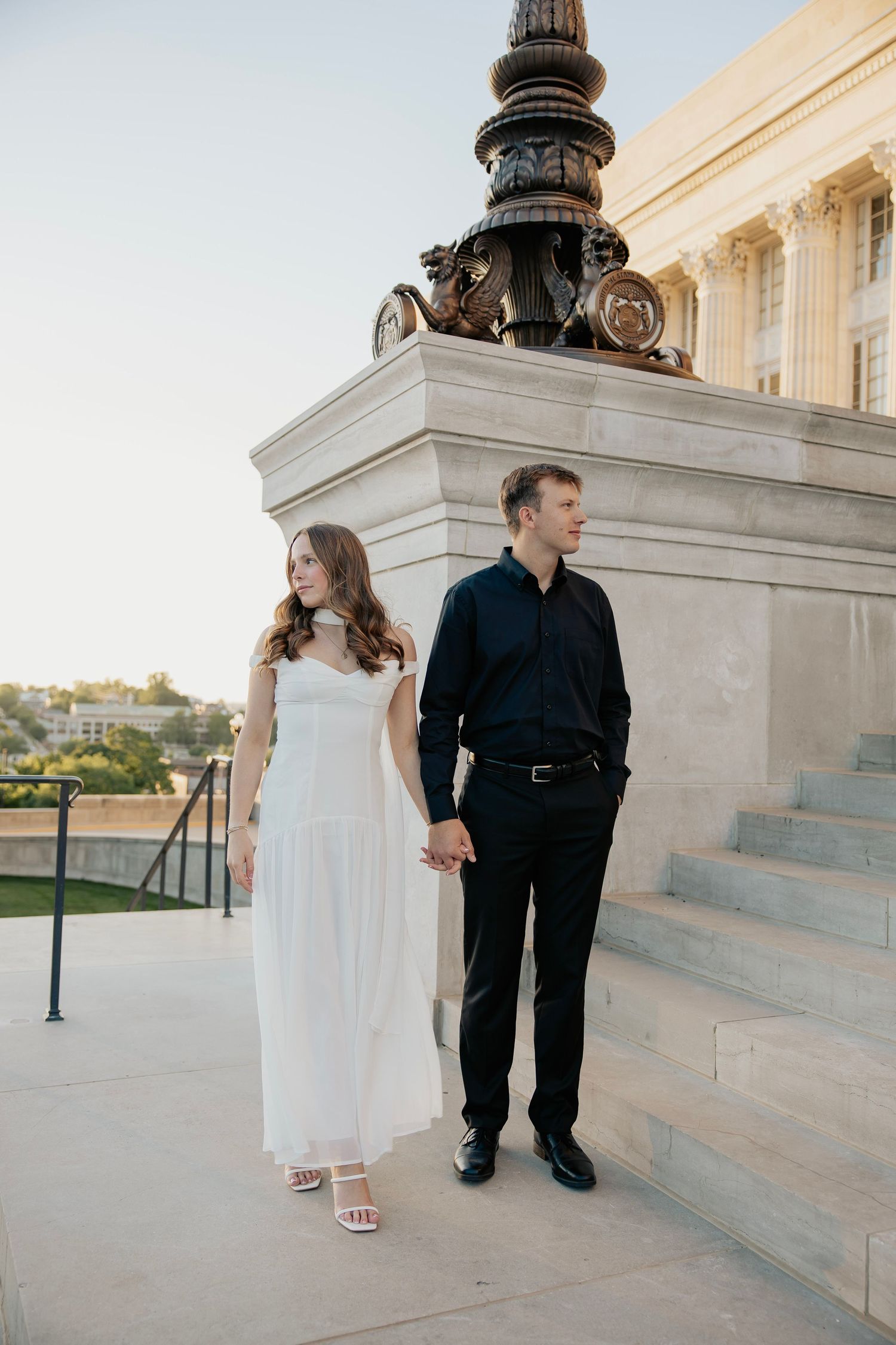 Couple holding hands near an ornate lamp post at a neoclassical building during golden hour.
