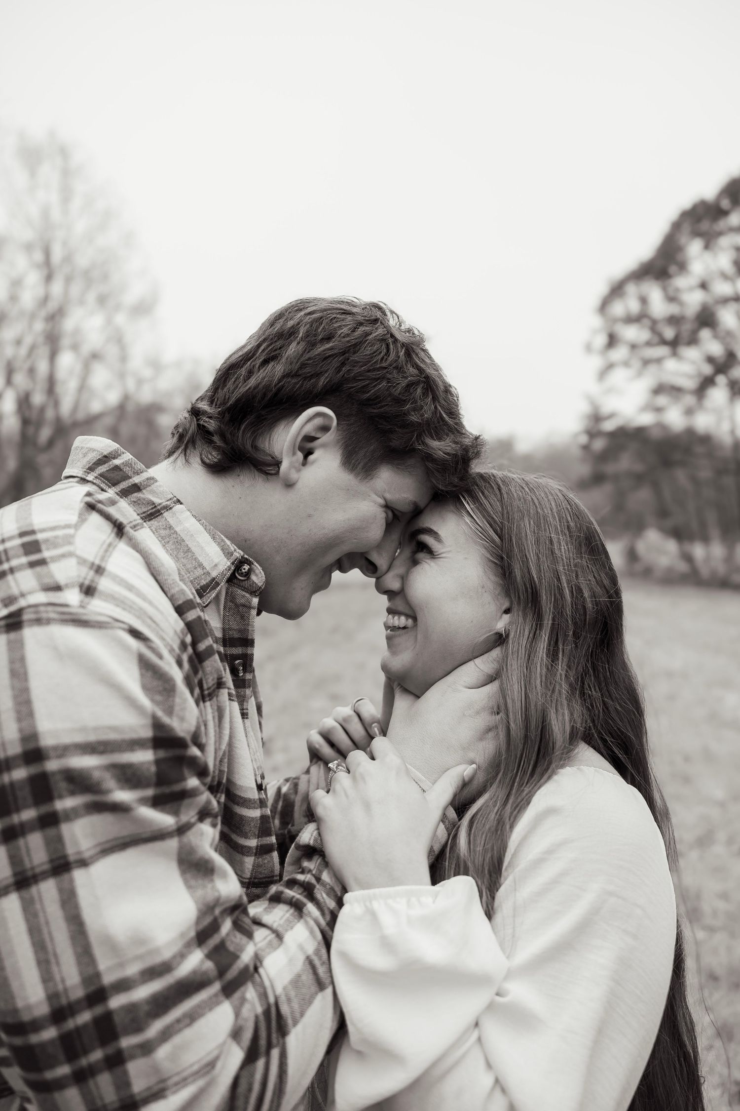 Happy couple touching foreheads and smiling in black and white outdoor engagement photo.