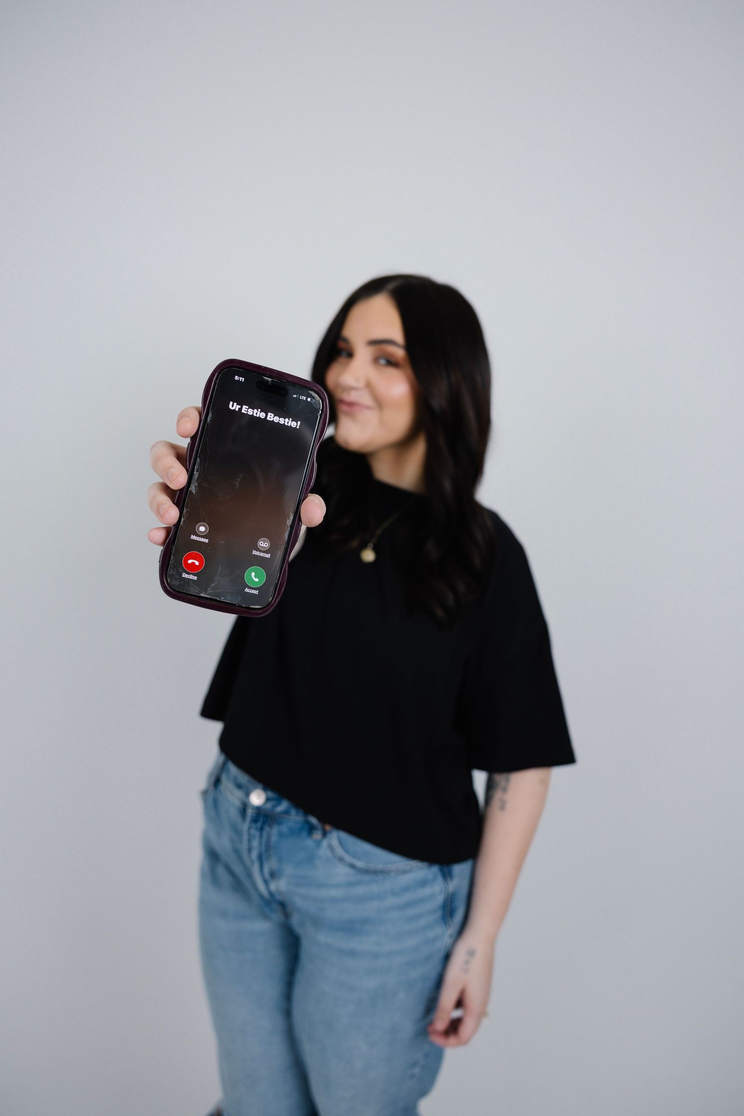 Smiling brunette woman in black tee holding up a smartphone showing an incoming call screen.