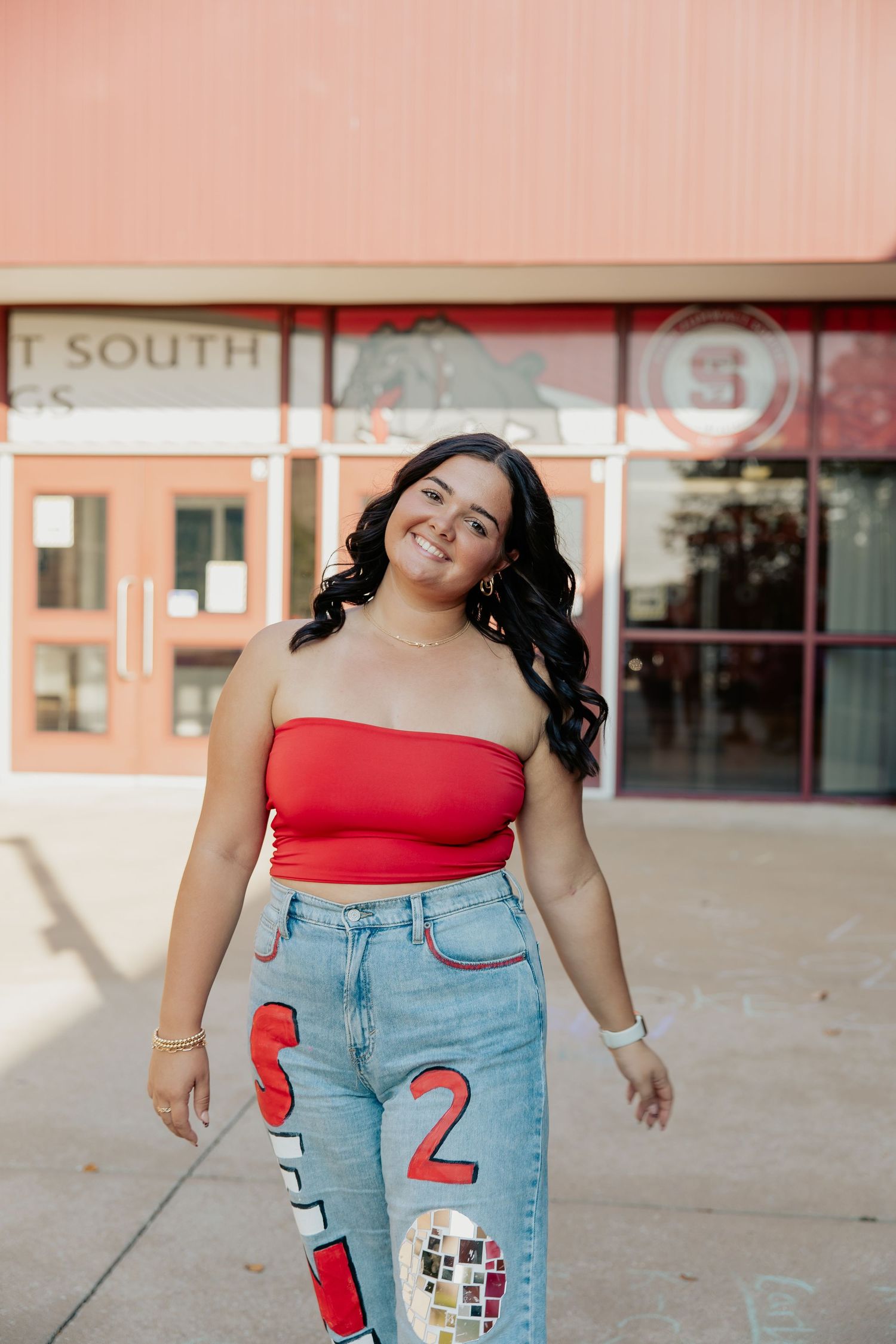 Smiling young woman in red tube top and custom senior jeans posing outside South high school.