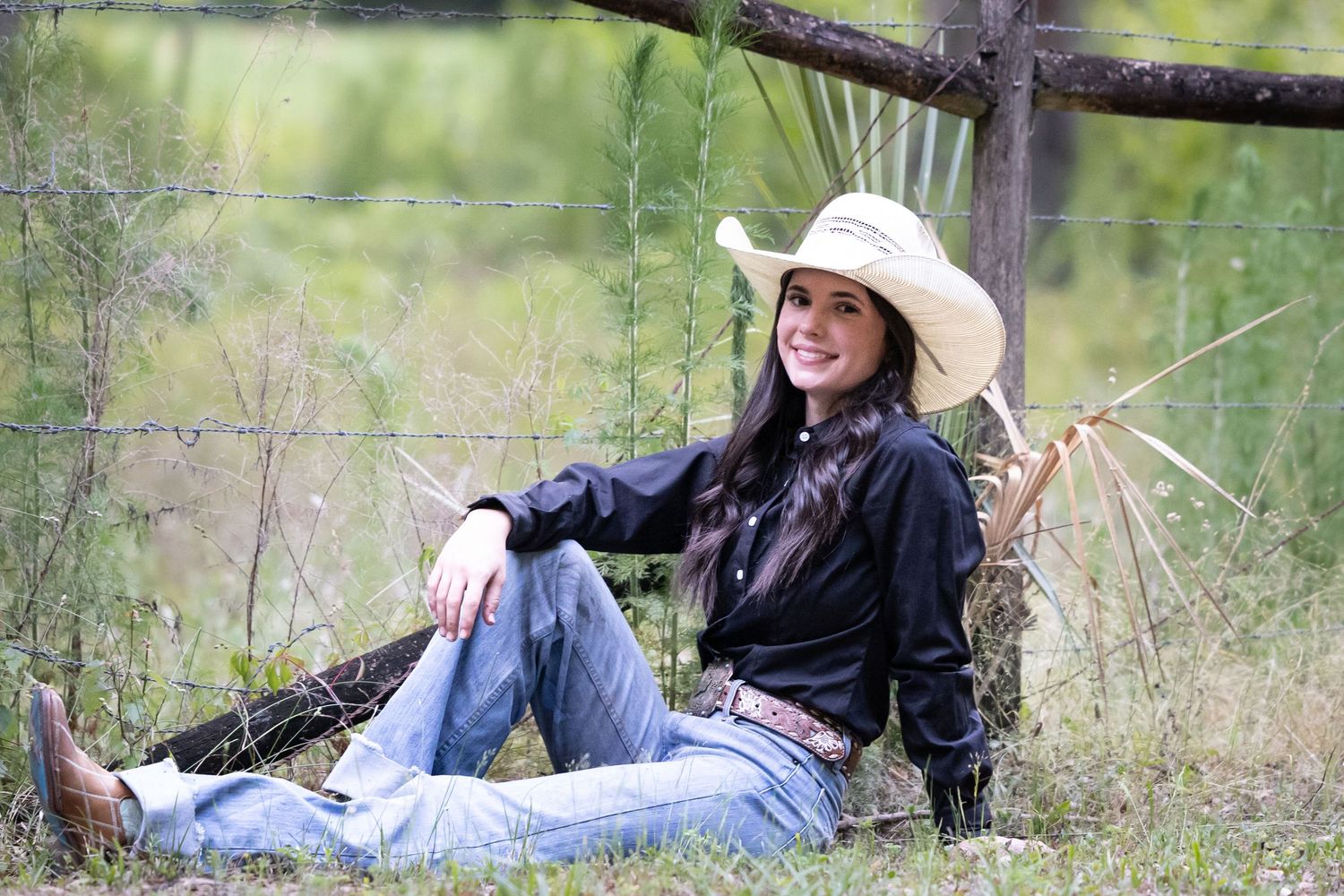 Senior graduate during a portrait session  relaxing outdoors in casual western wear against a natural backdrop. Keli Wakeley Photography