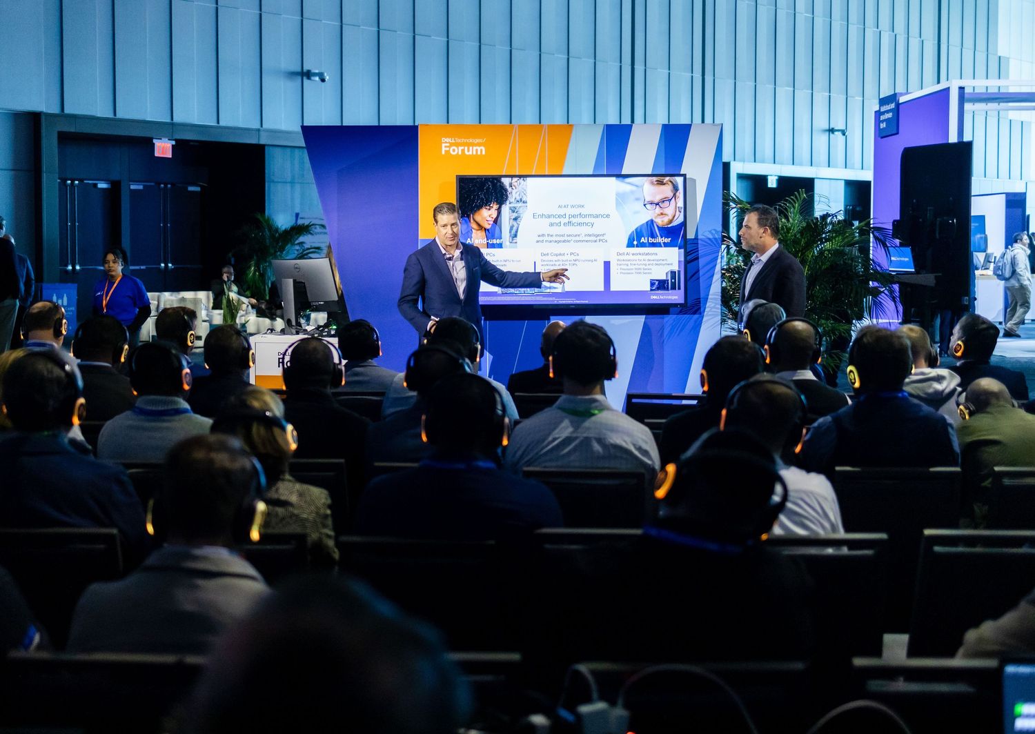 A speaker presents to an audience in a dimly lit auditorium with blue and yellow stage lighting during a business event photography in NYC.