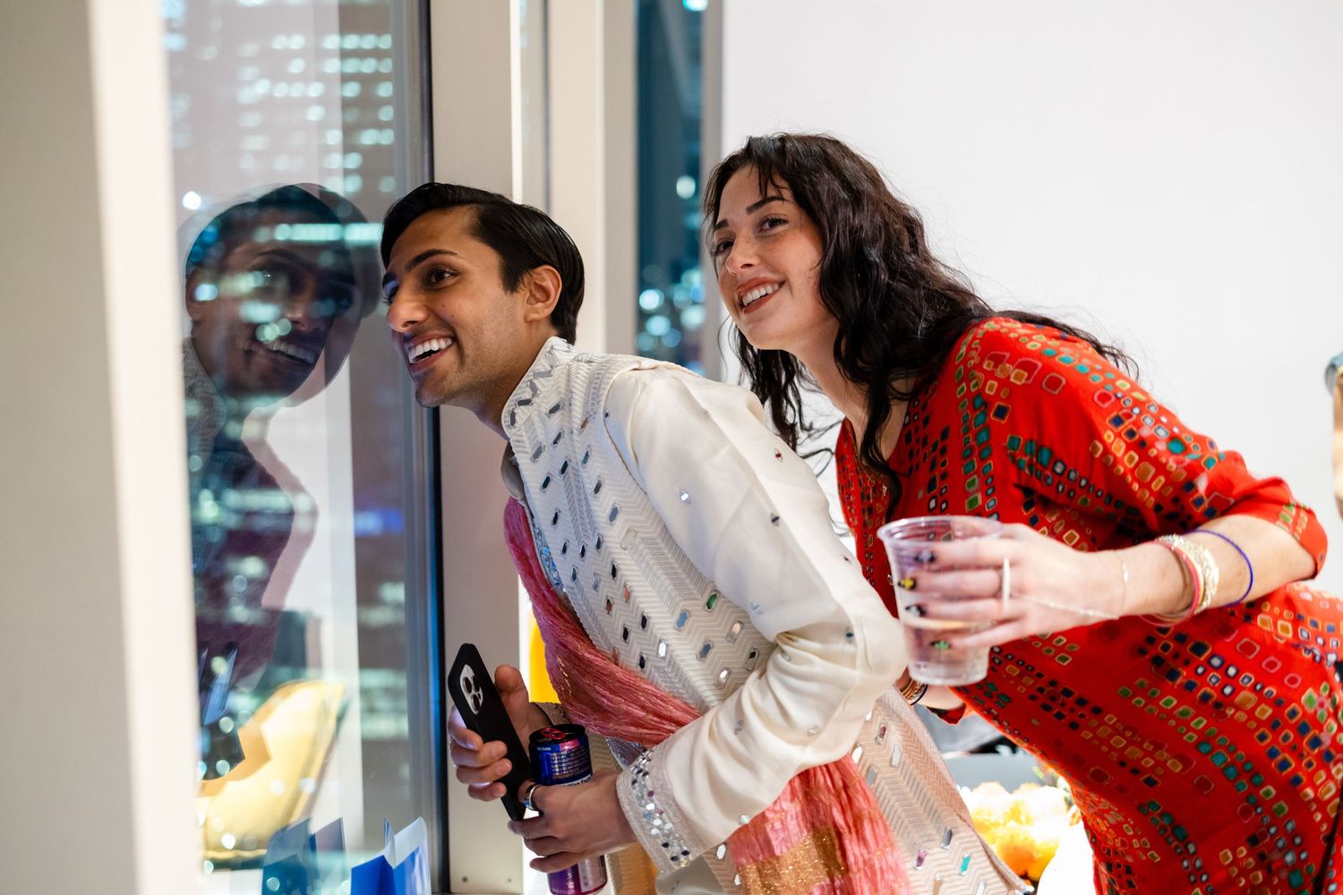 Two people in festive attire laugh together while playing arcade games at an entertainment venue.