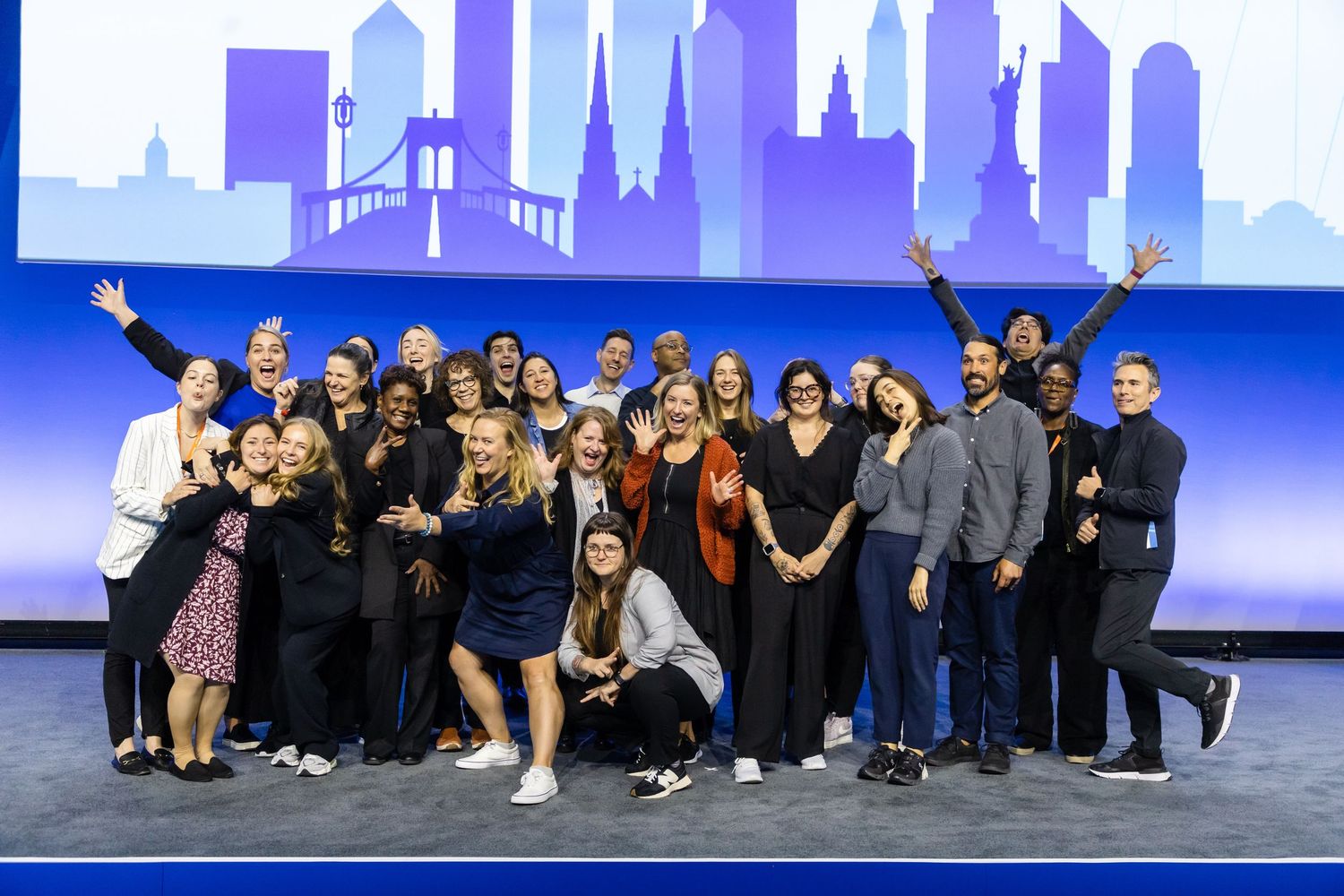 Excited team posing on stage at a corporate event in New York City, with a city skyline backdrop.