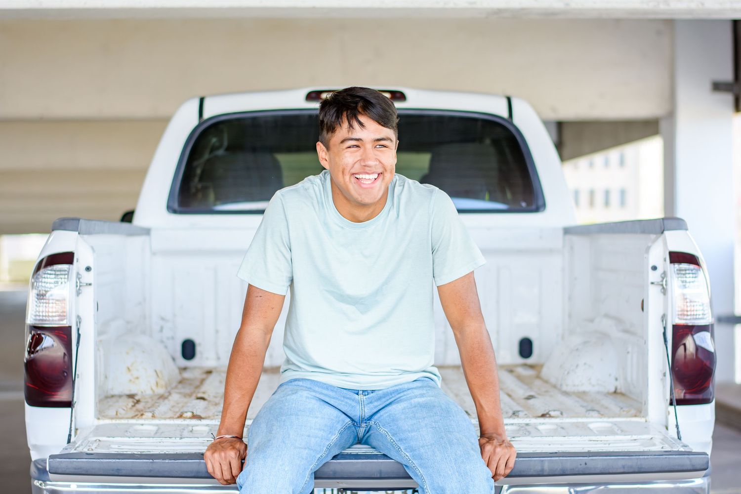 Casual senior portrait of student sitting outdoors in light blue shirt and jeans.
