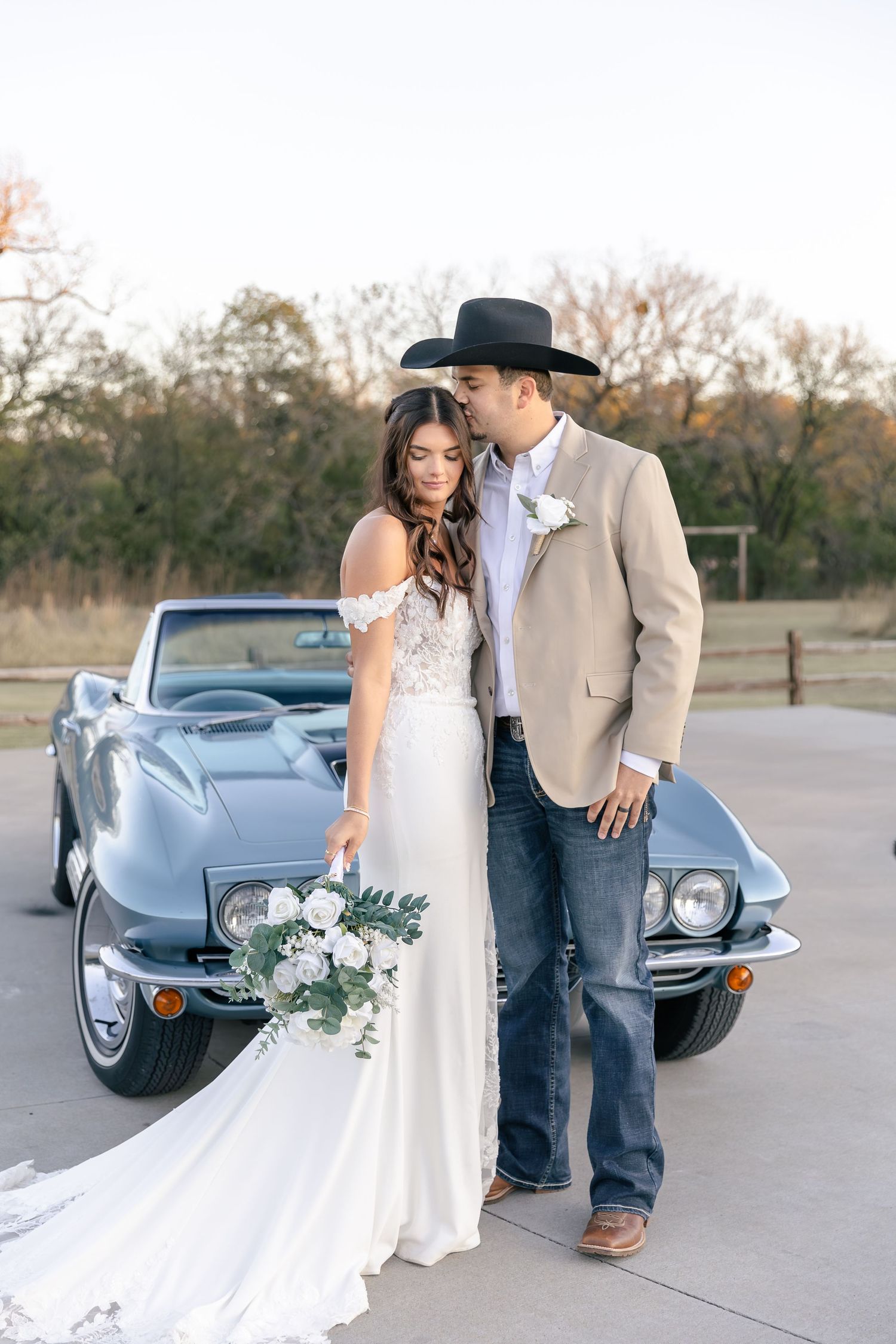 Wedding couple poses beside a classic light blue vintage car at sunset.