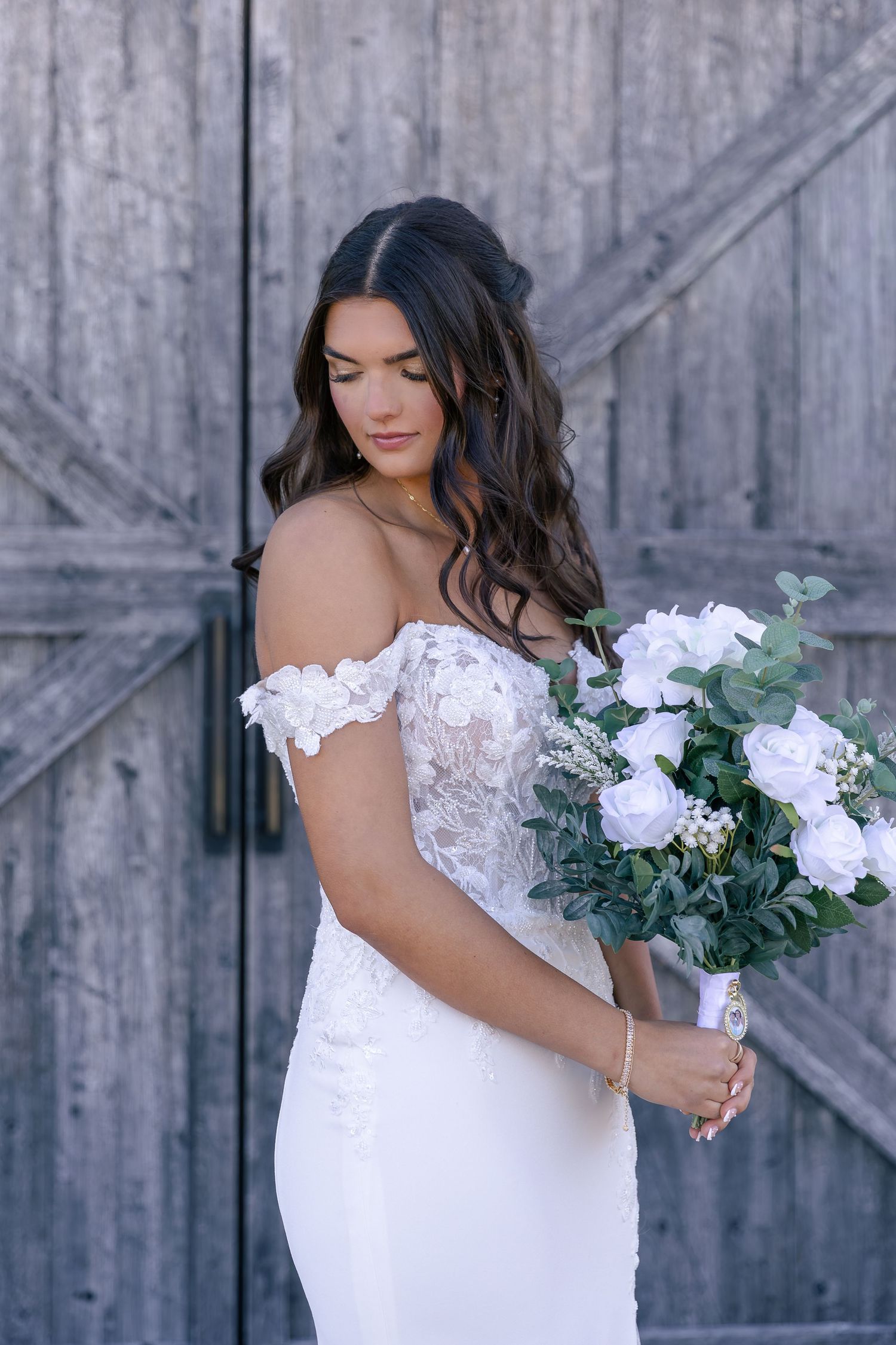 Close-up of a white lace wedding dress with delicate off-shoulder details against weathered wood.