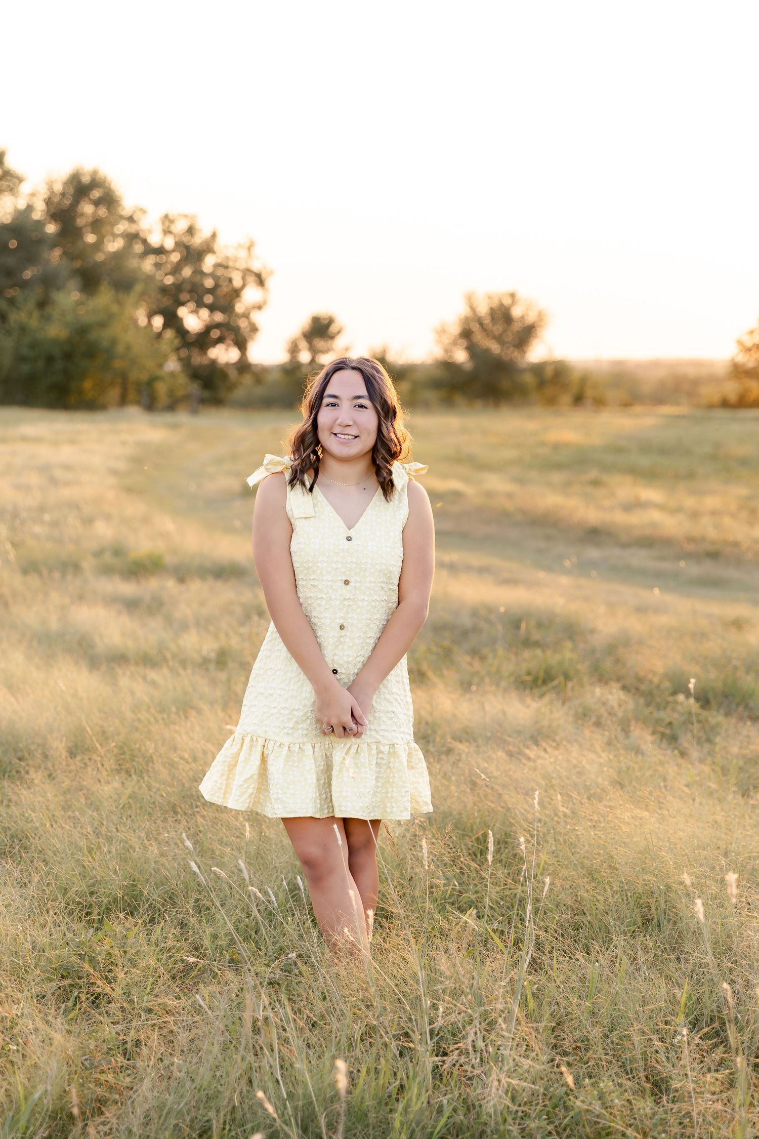 A white summer dress senior photoshoot in a sunlit field during golden hour.