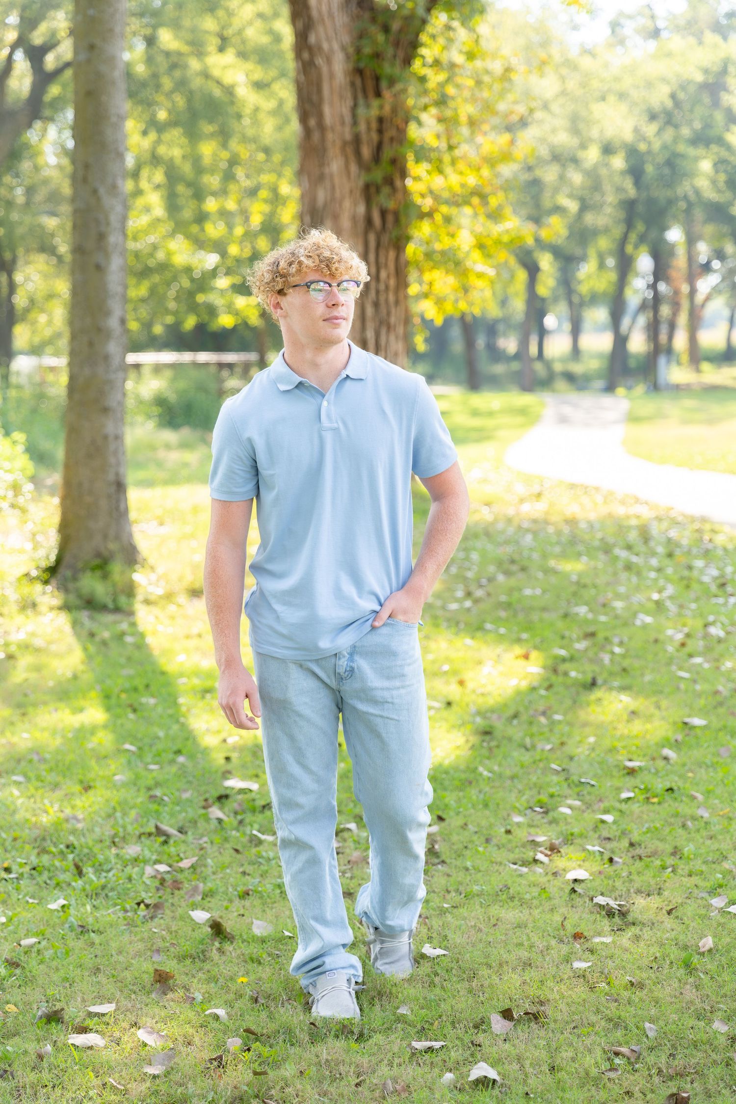 A series of casual senior boy poses in a light blue outfit against a sunny park background with fallen leaves.