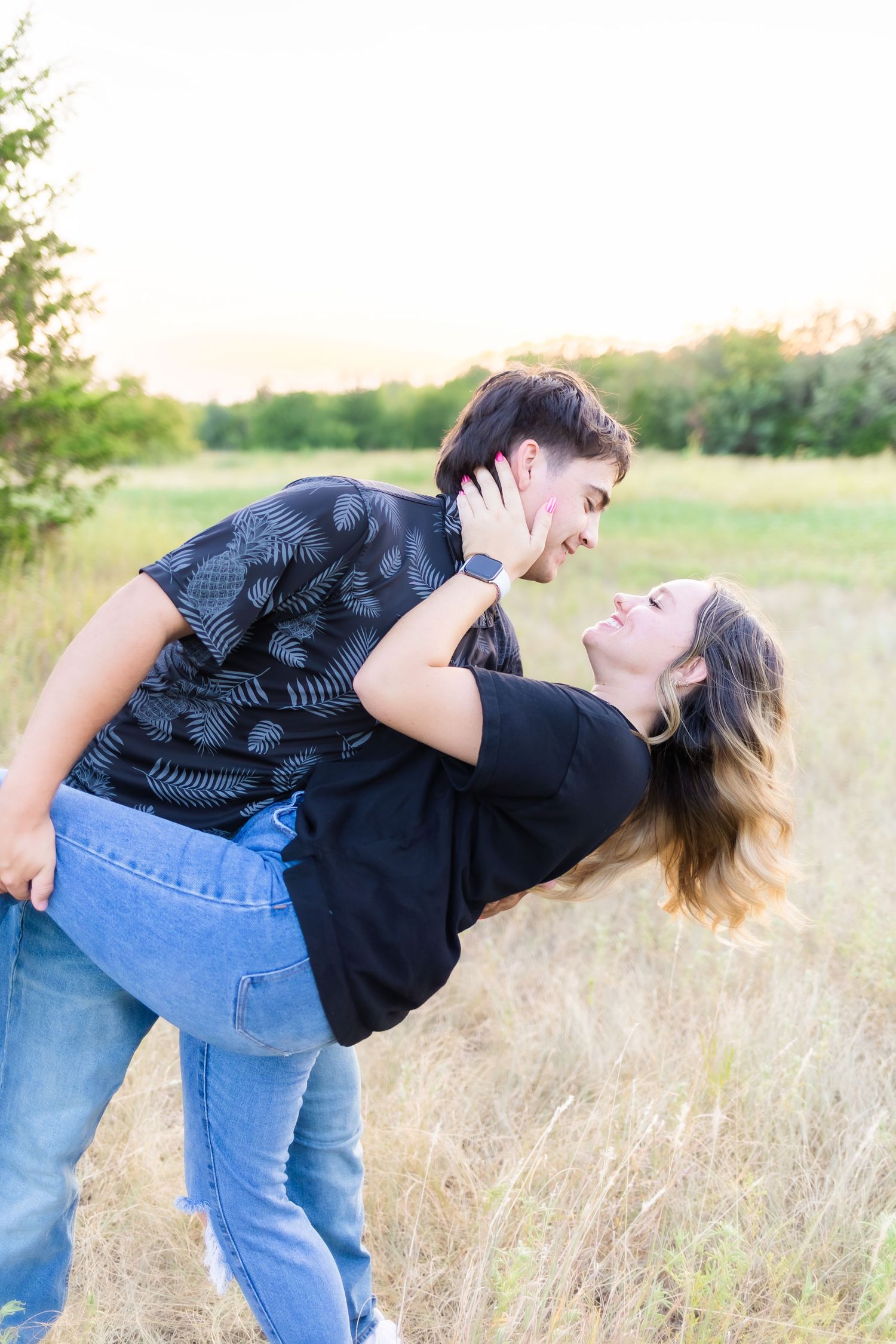 Playful couple in casual attire dancing and dipping in a golden sunlit field.