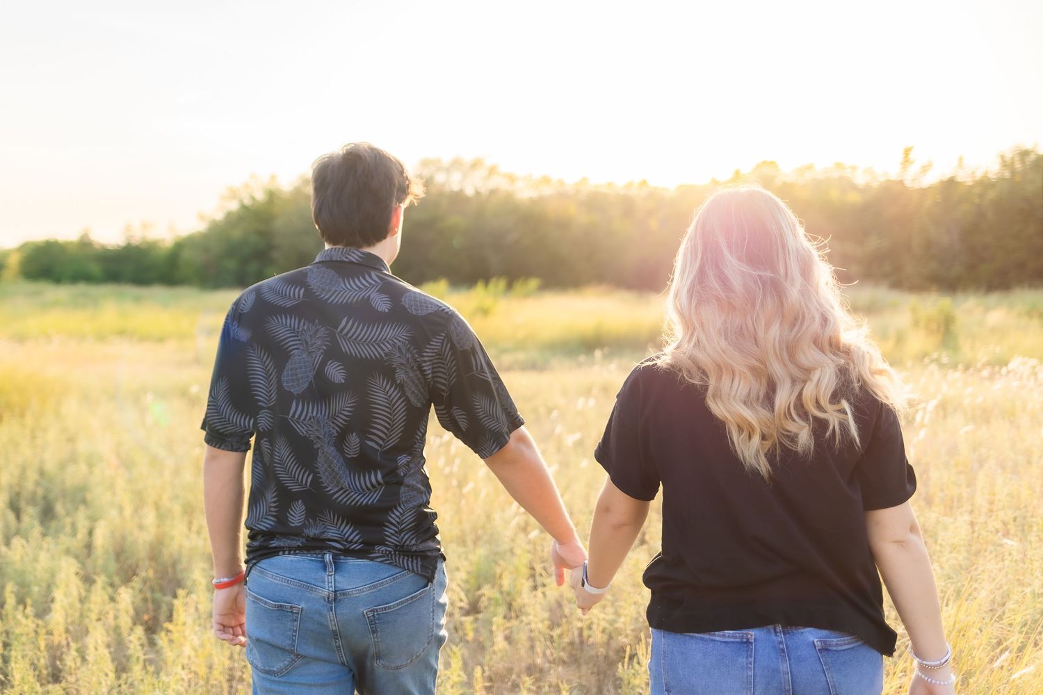Silhouetted couples walking hand in hand through a sun-drenched field at golden hour.