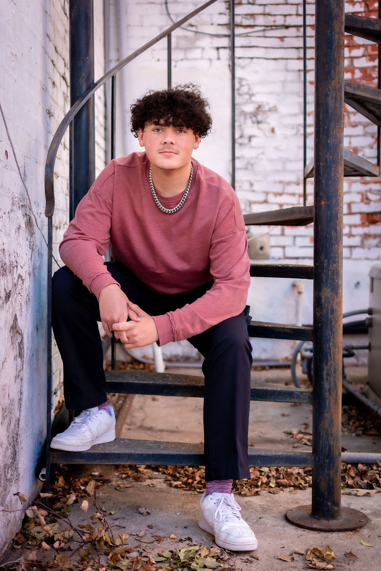 Senior portrait featuring student in burgundy sweater sitting on industrial steps.