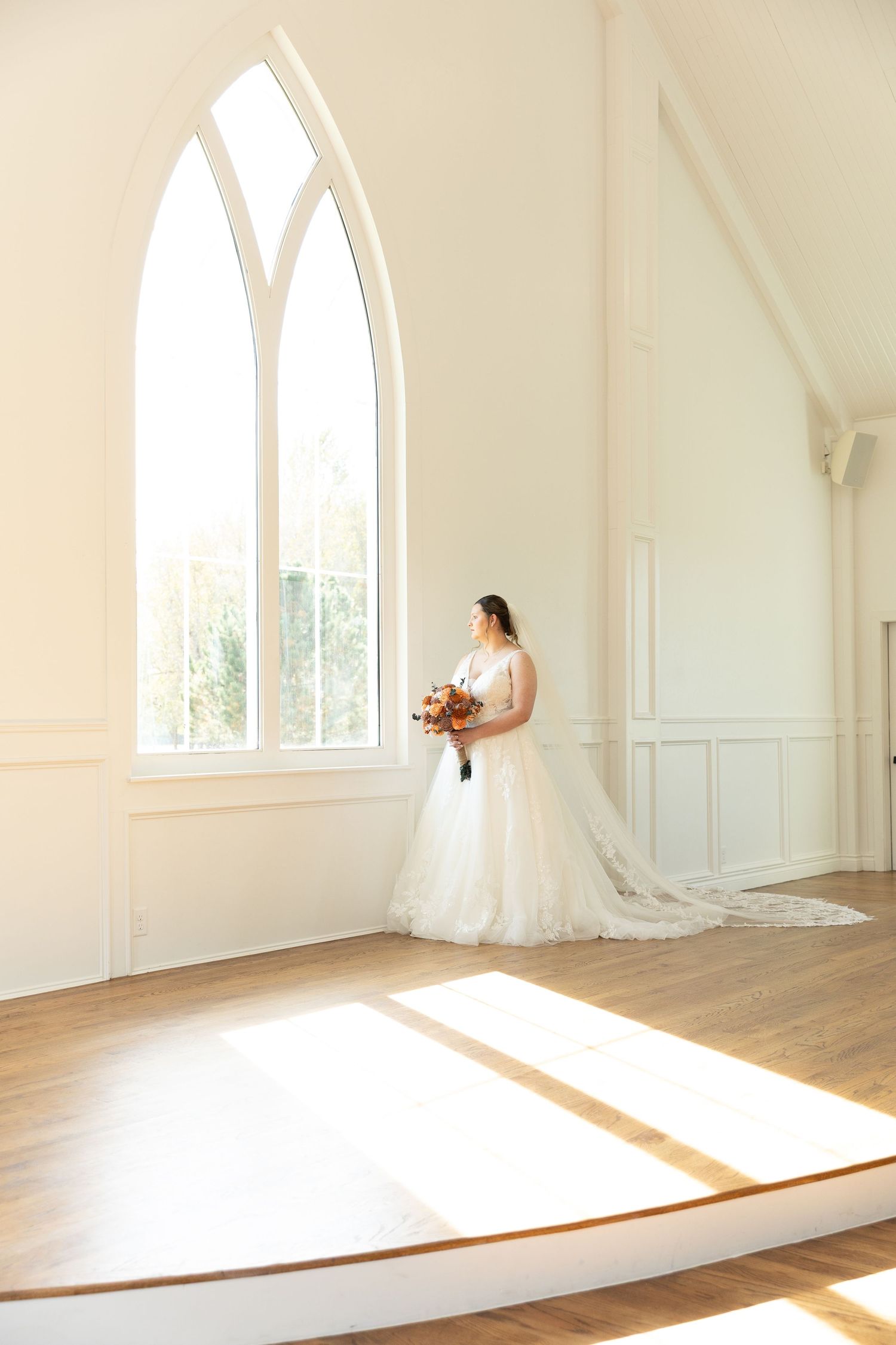 Sunlight streams through arched chapel windows onto a hardwood floor creating dramatic shadows.