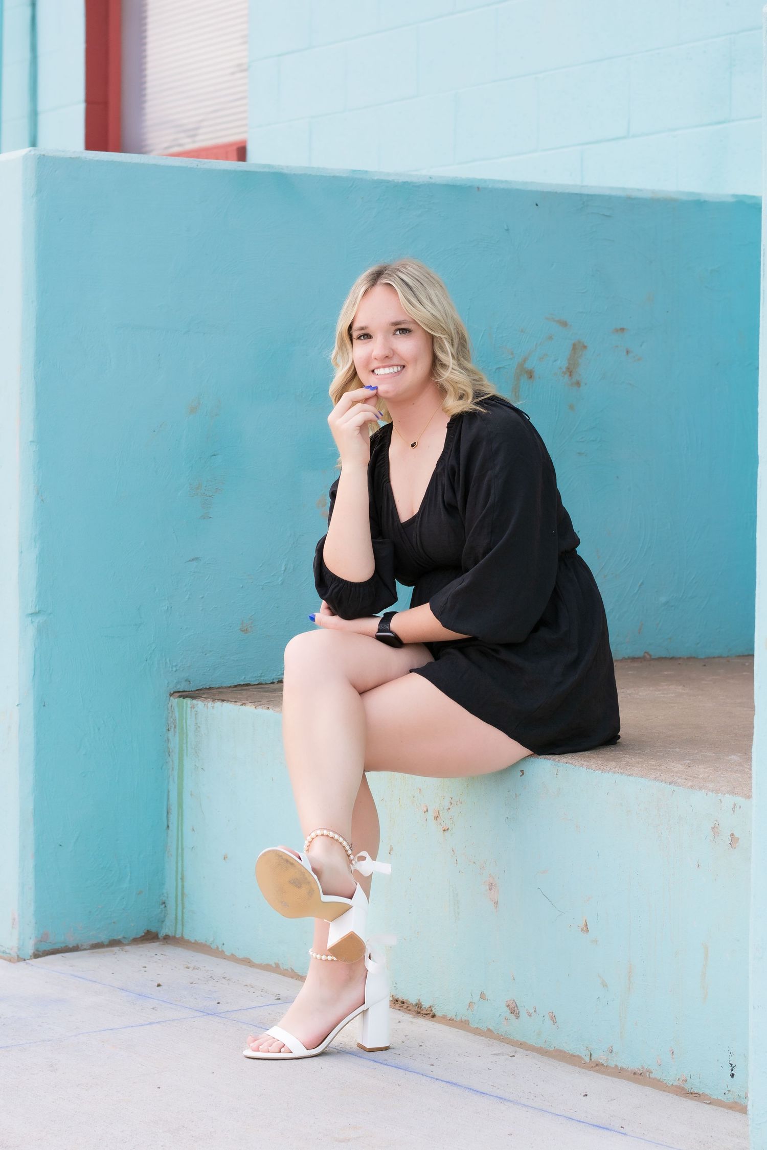 Senior Fashion poses against a light blue wall wearing a black outfit and white heels.