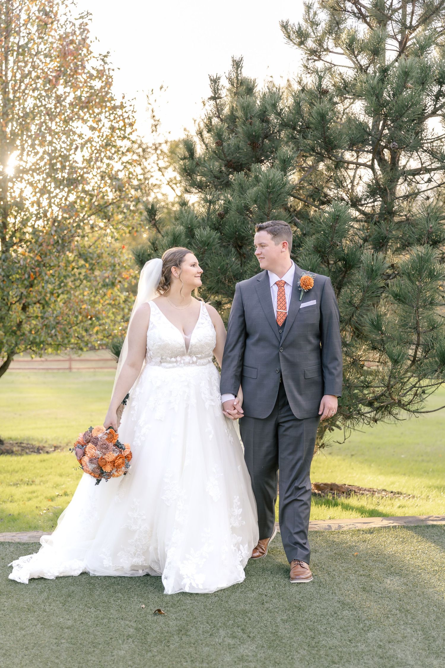 Wedding couple poses in an outdoor garden setting with fall foliage in the background.