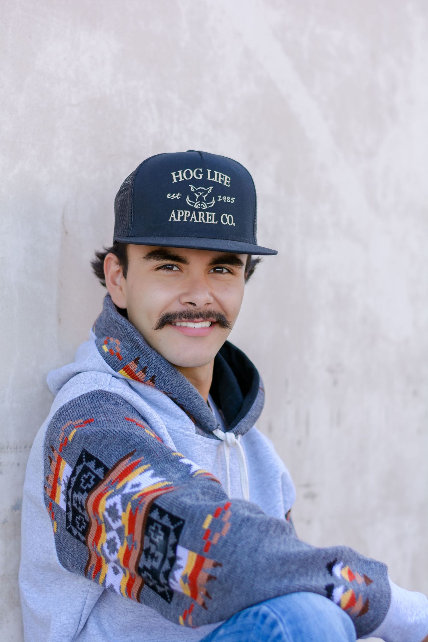 Senior Portrait series wearing Hog Life baseball cap and patterned hoodie against a light background.